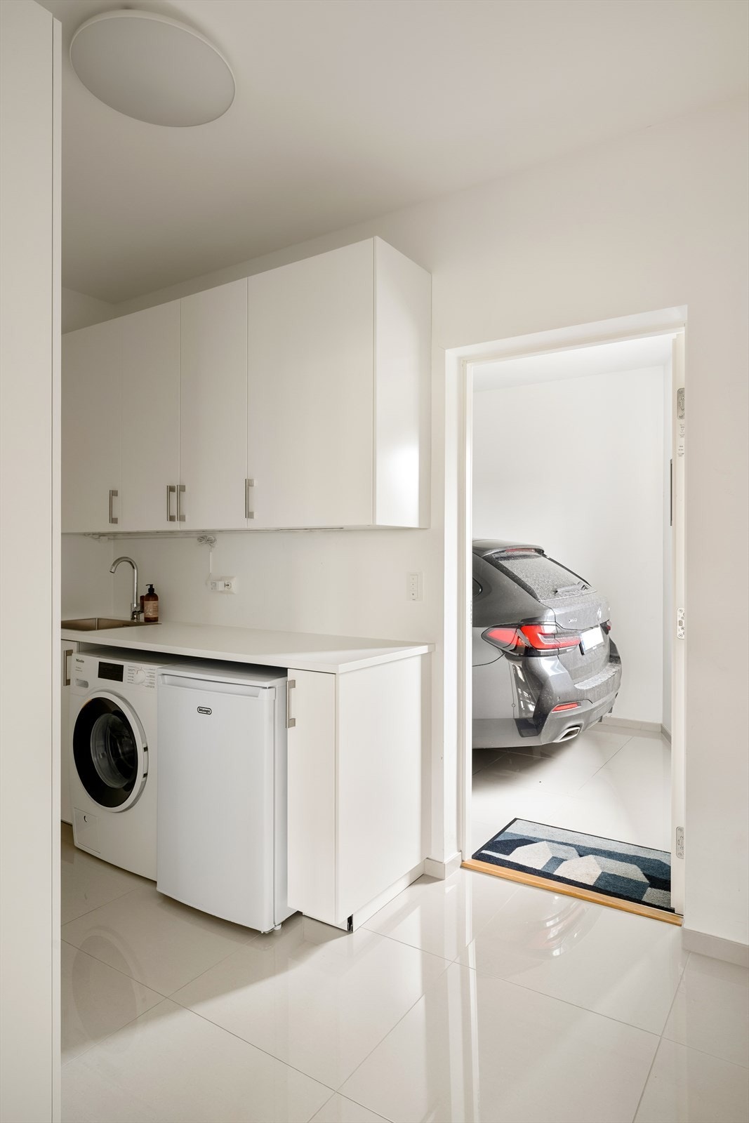 Vaskerommet har flislagt gulv og lyse veggflater, og leder videre inn til den integrerte garasjen - også denne med store fliser og lyse overflater. Galleribilde