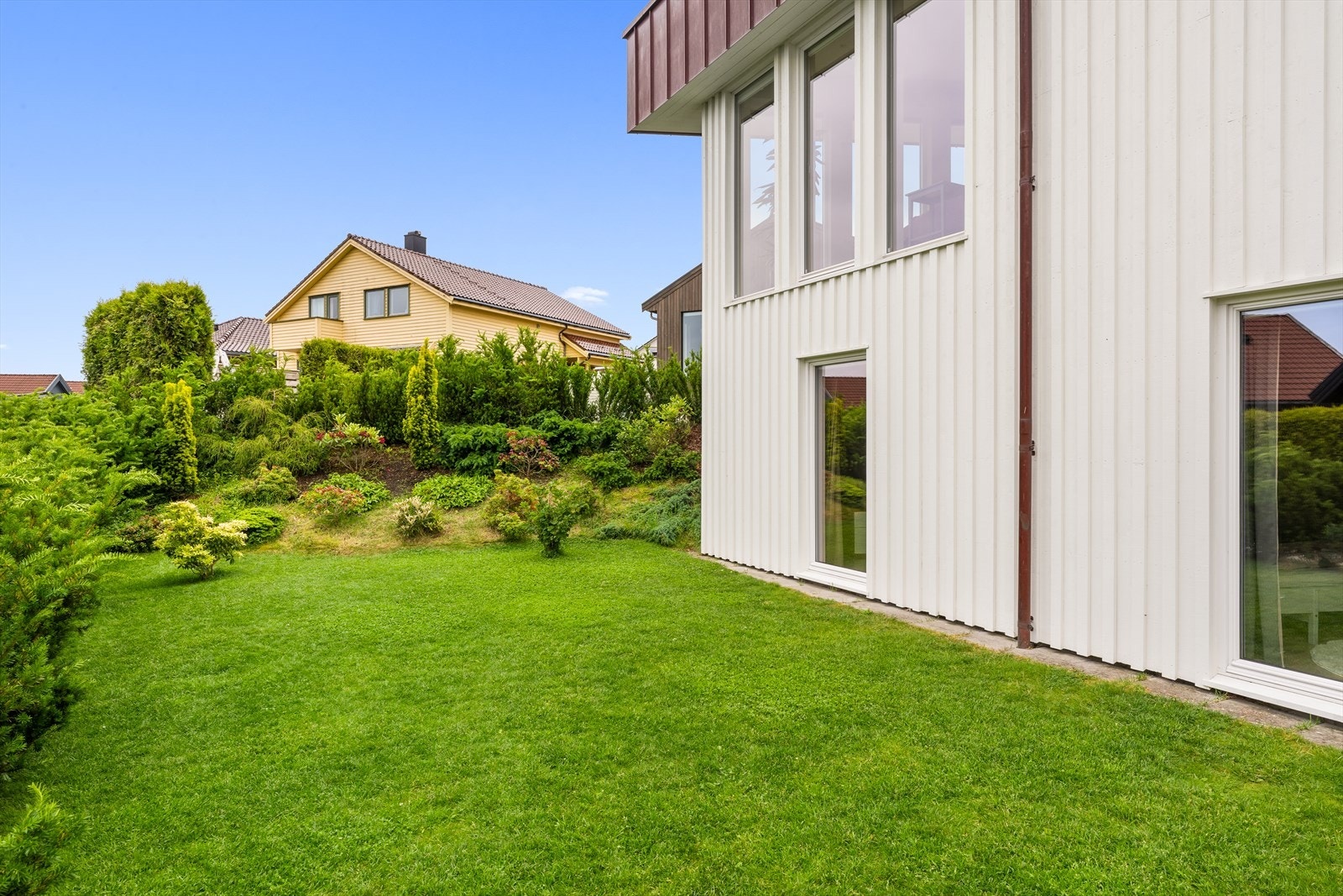 Hagen er anlagt med velstelt plen, tettvokst hekk og vakre prydbusker som skaper en grønn og innbydende ramme rundt boligen. Galleribilde
