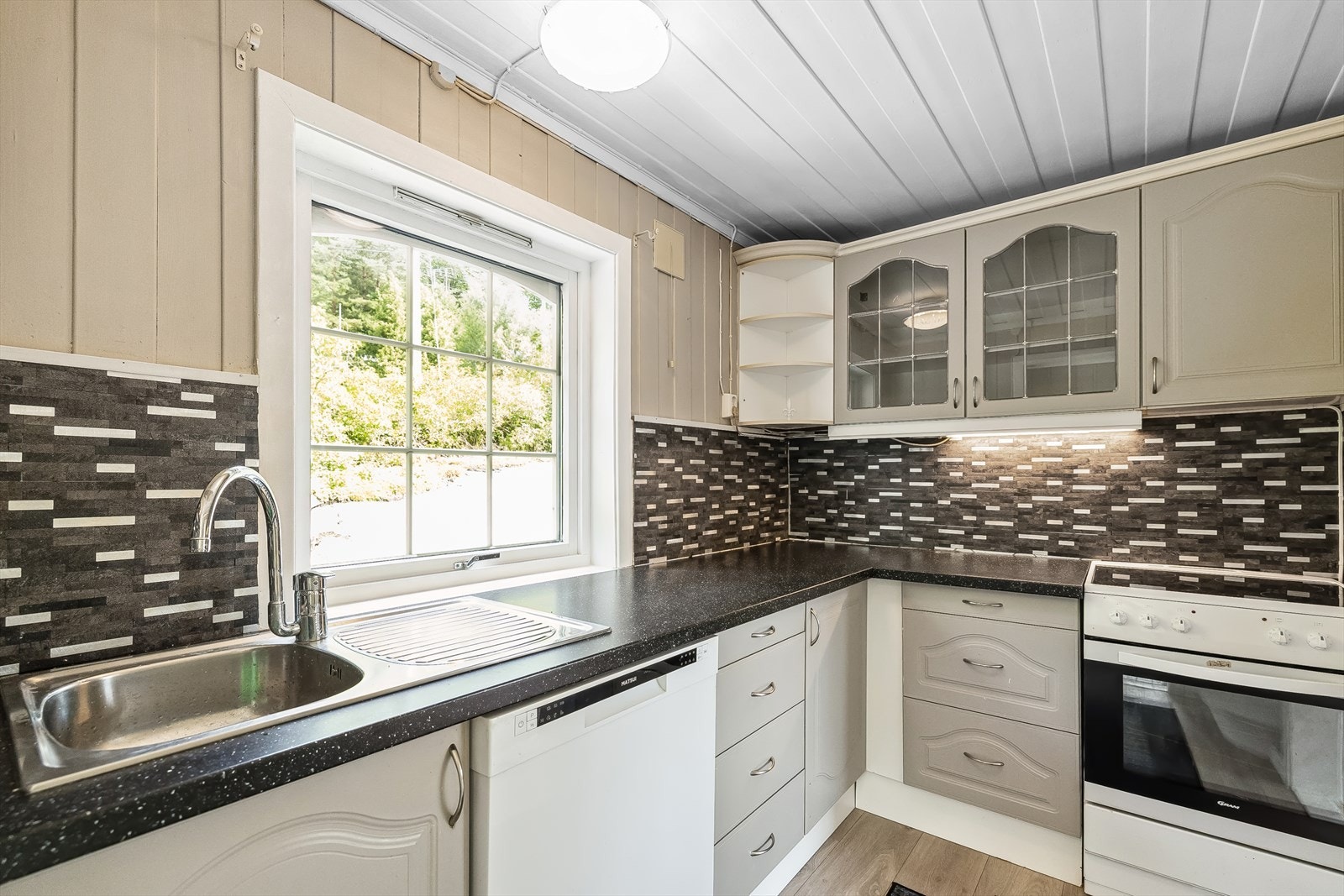 Hytta har et delvis åpent kjøkken med en innredning med profilerte fronter, enkelte glassfronter i overskap, laminat benkeplate med nedfelt kum i rustfritt stål, vinylfliser på vegg over benkeskap og belysning under overskap. Galleribilde