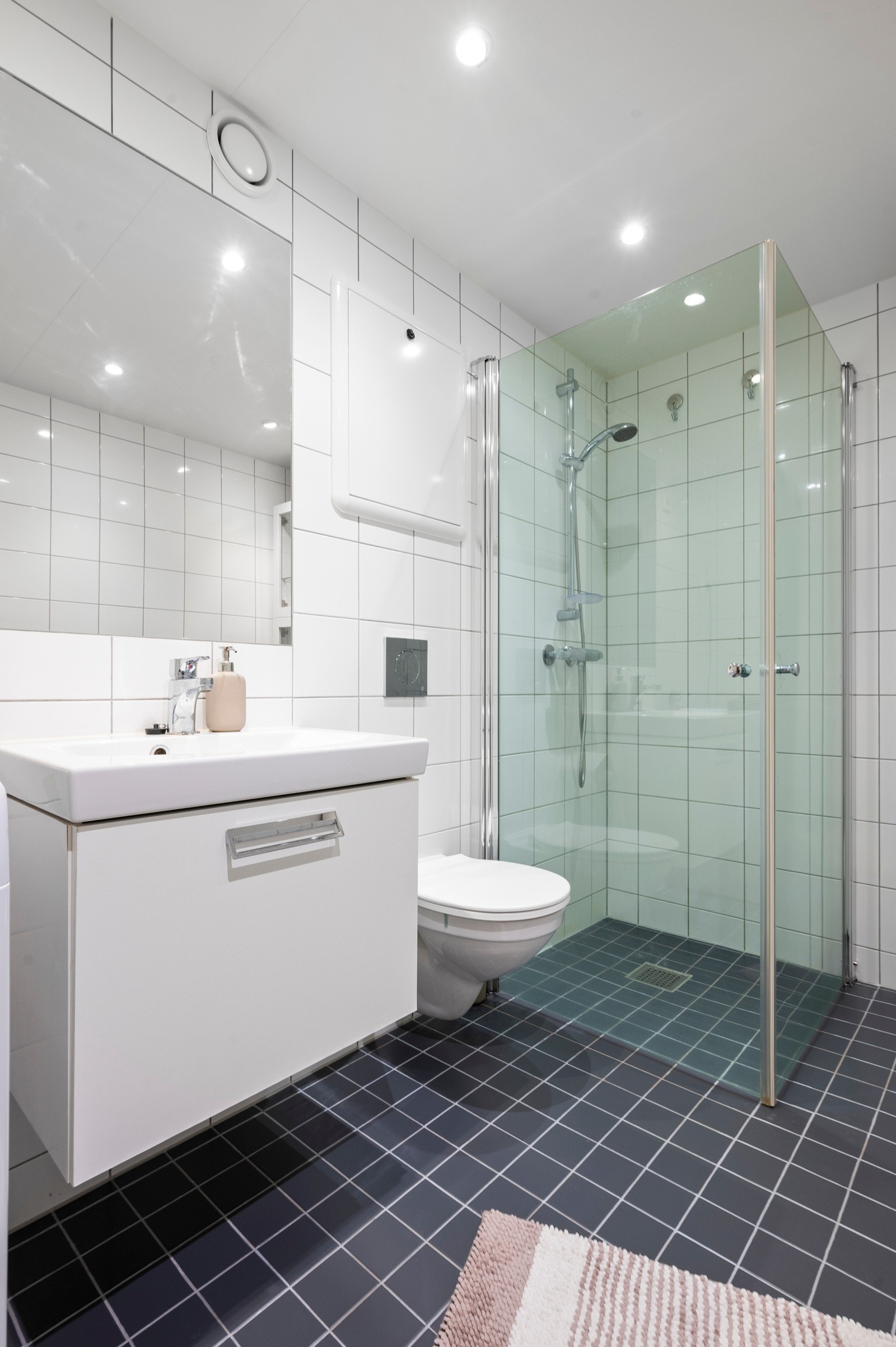 Badet er utstyrt med vegghengt toalett og dusjhjørne med innfellbare glassdører i herdet glass Galleribilde