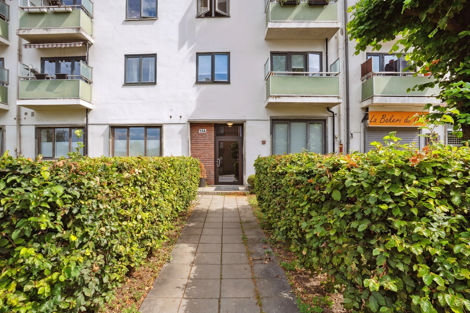 Inngangsparti med grøntareal. Bakeri med fransk sjel i nabobygget. Her kan du nyte bakeverk fra øverste hylle Galleribilde