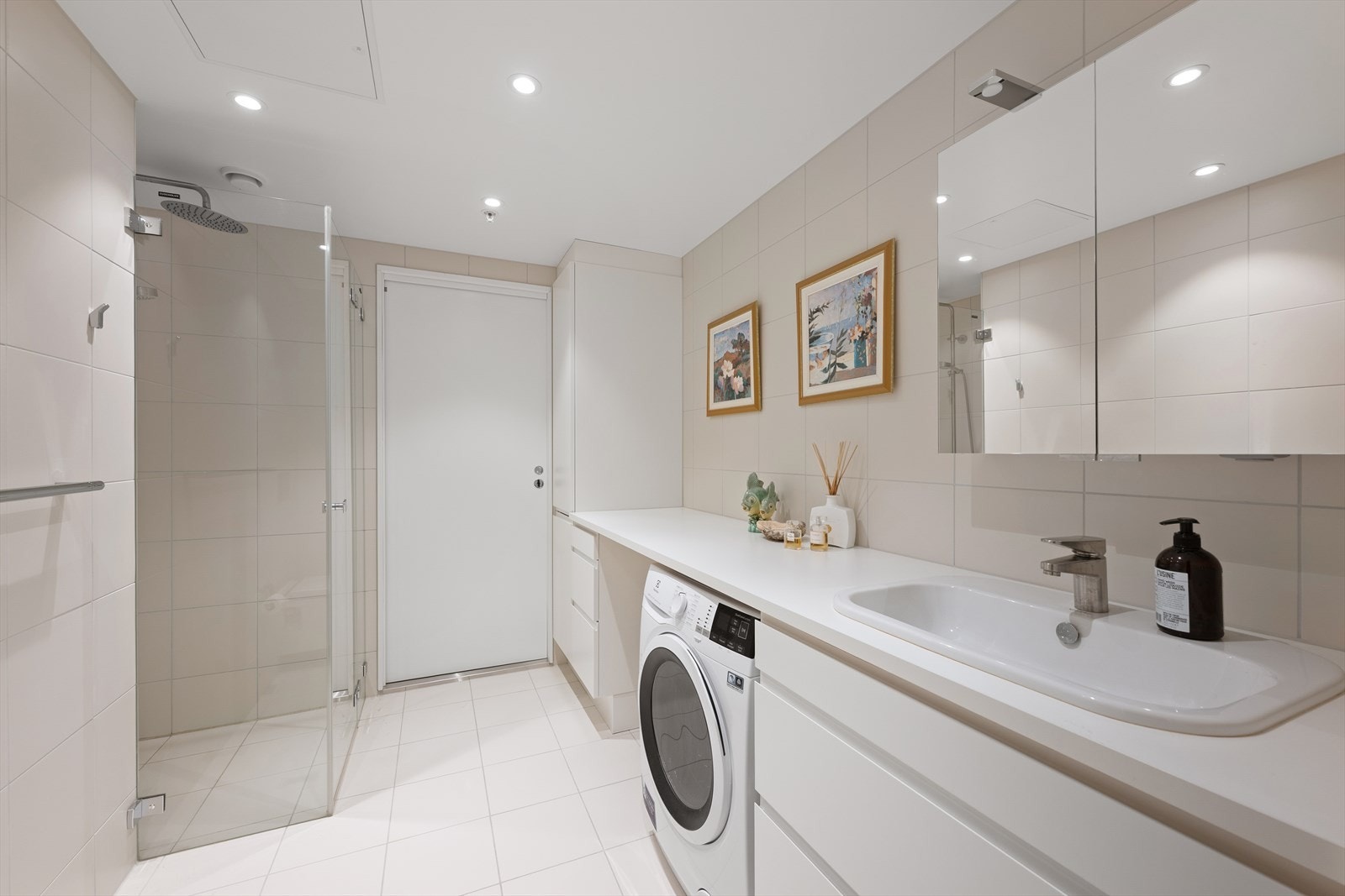 Badet er innredet med veggmontert toalett, servant, dusjhjørne og opplegg for vaskemaskin Galleribilde