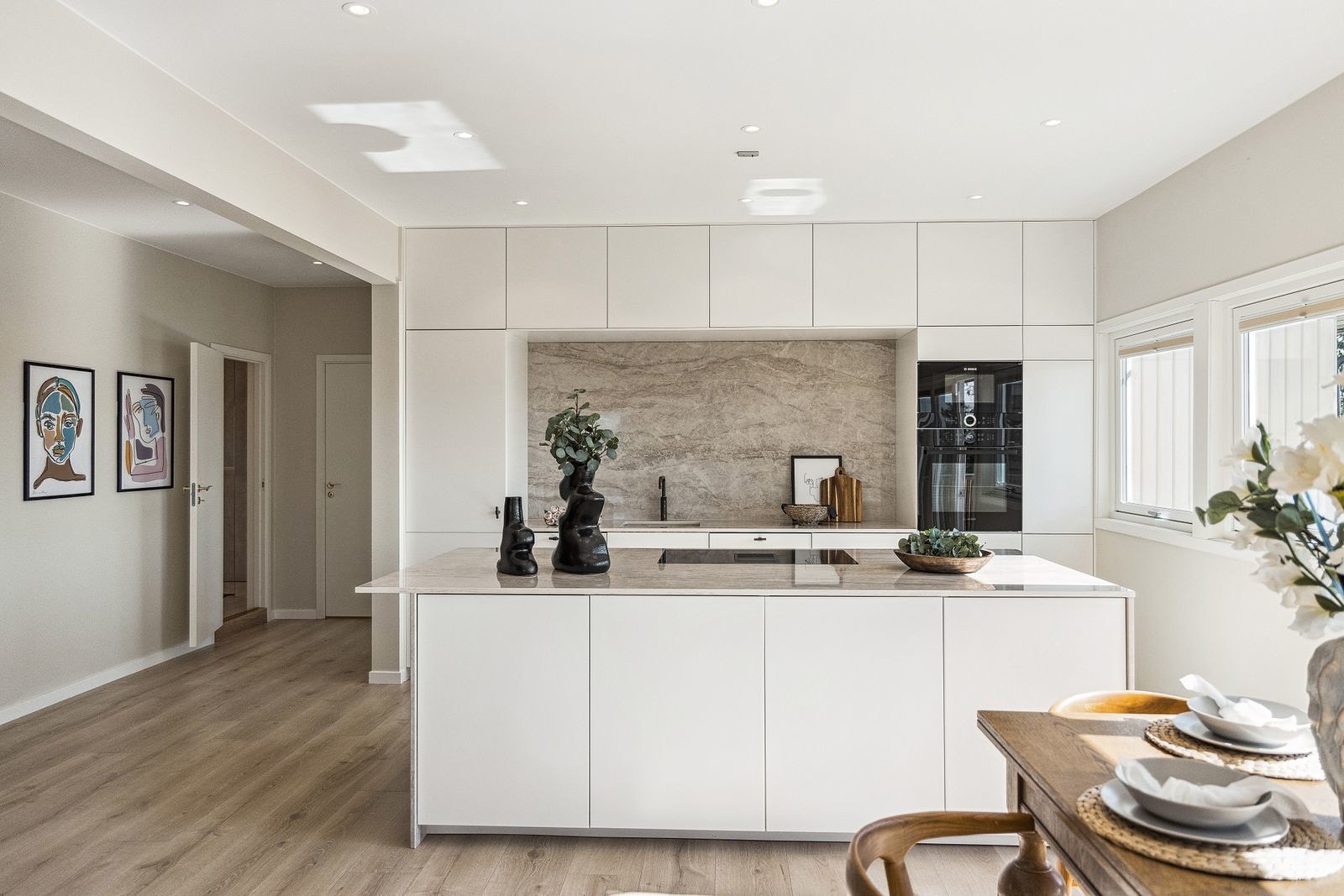 Kjøkkeninnredningen med hvite slette fronter og benkeplater av stein, lekker steinplate som pryder og beskytter bakveggen Galleribilde