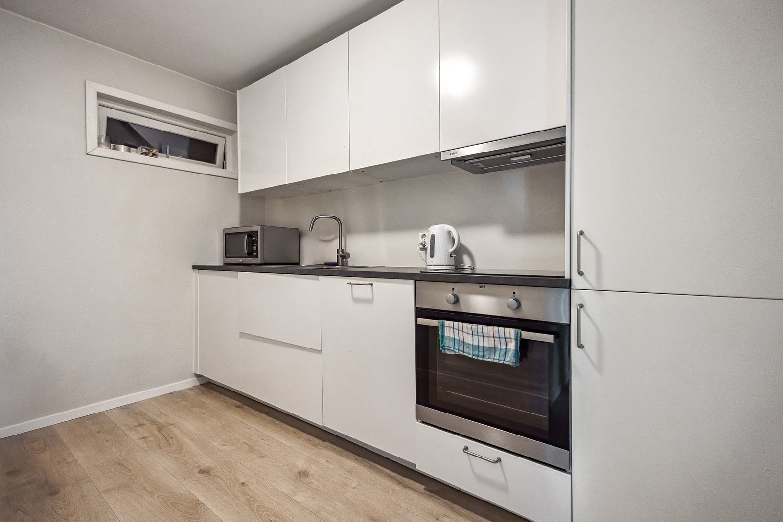 Kjøkkeninnredning med slette fronter og laminert benkeplate. I innredningen er det integrert stekeovn, platetopp og oppvaskmaskin. Ventilatoren har kullfilter. Galleribilde