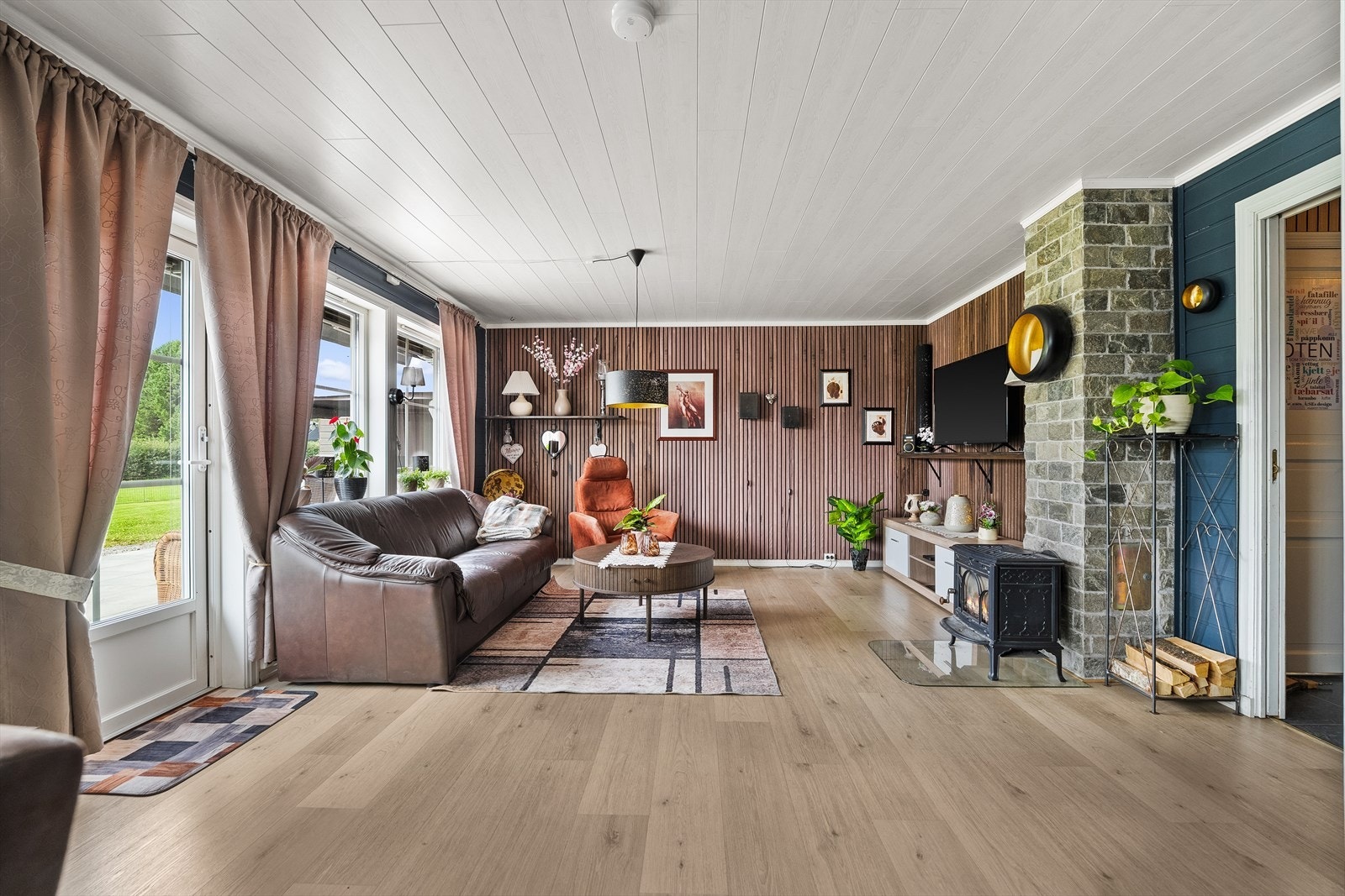 Koselig stue del med sofa og tv-krok. Moderne spiler på to vegger gir et moderne uttrykk. Peisovn for oppvarming. Galleribilde