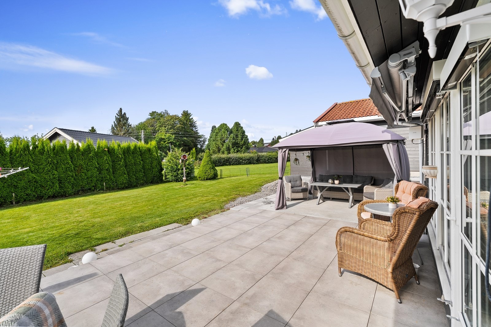 Uteplassen er innredet i flere soner. Pergola mot garasje og terrassemarkise gjør at du kan benytte uteplassen i vær og vind og forlenge sesongen. Galleribilde