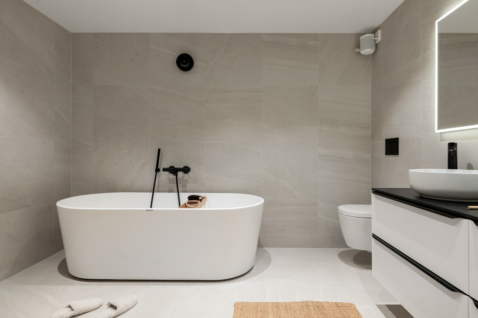 Badet er innredet med stor dusjsone, vegghengt toalett, badekar, baderomsinnredning med to servanter og speil med belysning. Galleribilde