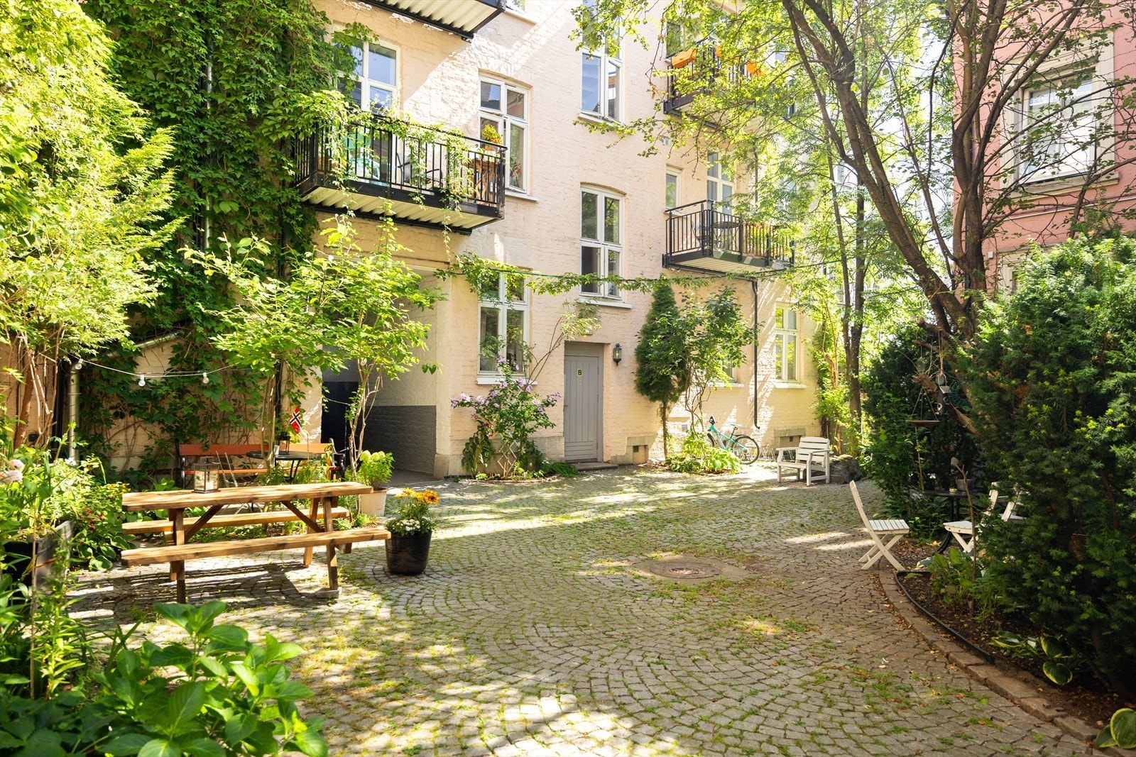 Idyllisk og skjermet bakgård som er pent opparbeidet med brostein, sittebenker og hyggelige grøntområder Galleribilde