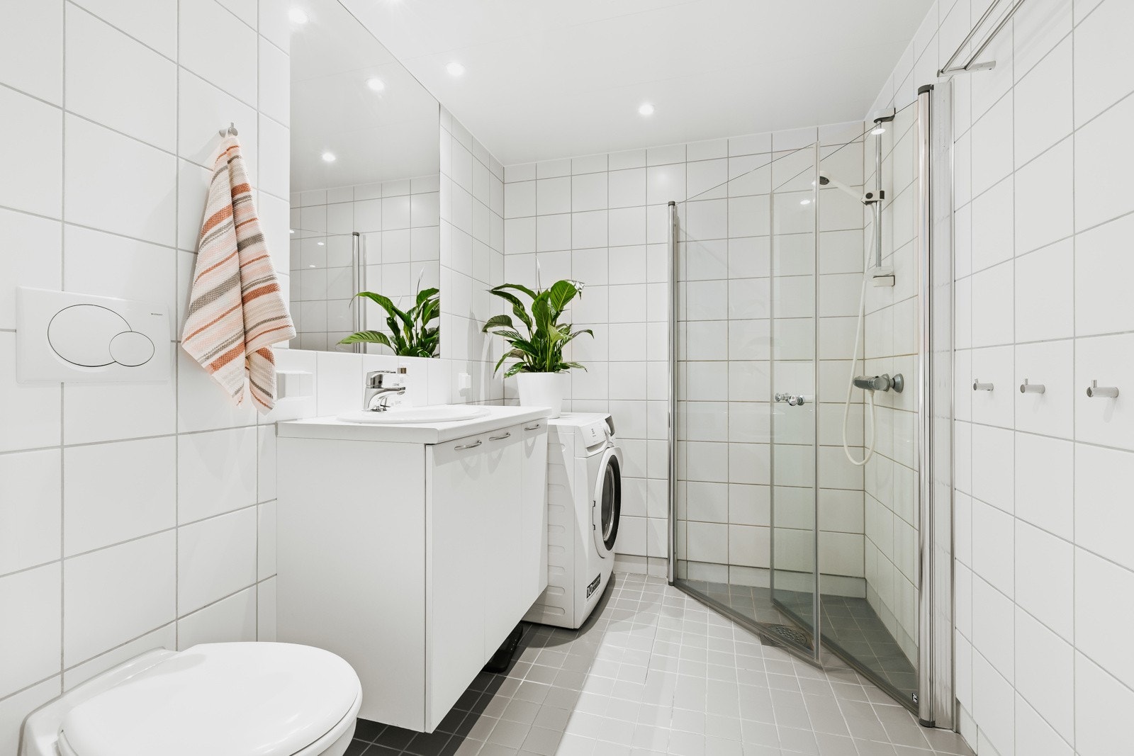 Flislagt baderom med gulvvarme, servant i benkeskap, dusjnisje med innfellbare glassdører og vegghengt toalett Galleribilde