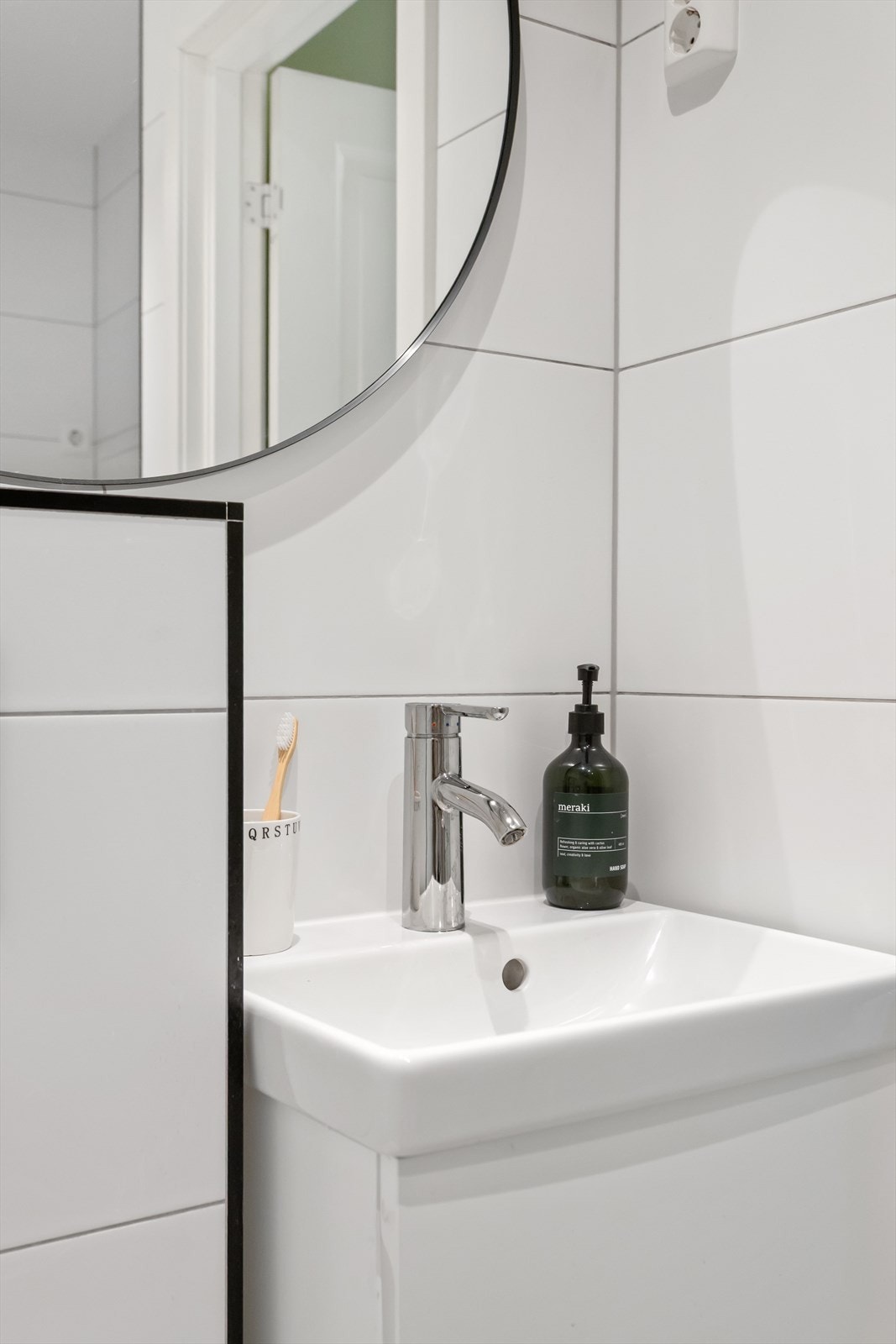 Baderomsinnredningen omfatter benkeskap med glatt front, speil over servant, servant og et veggmontert toalett med innebygget sisterne. Galleribilde