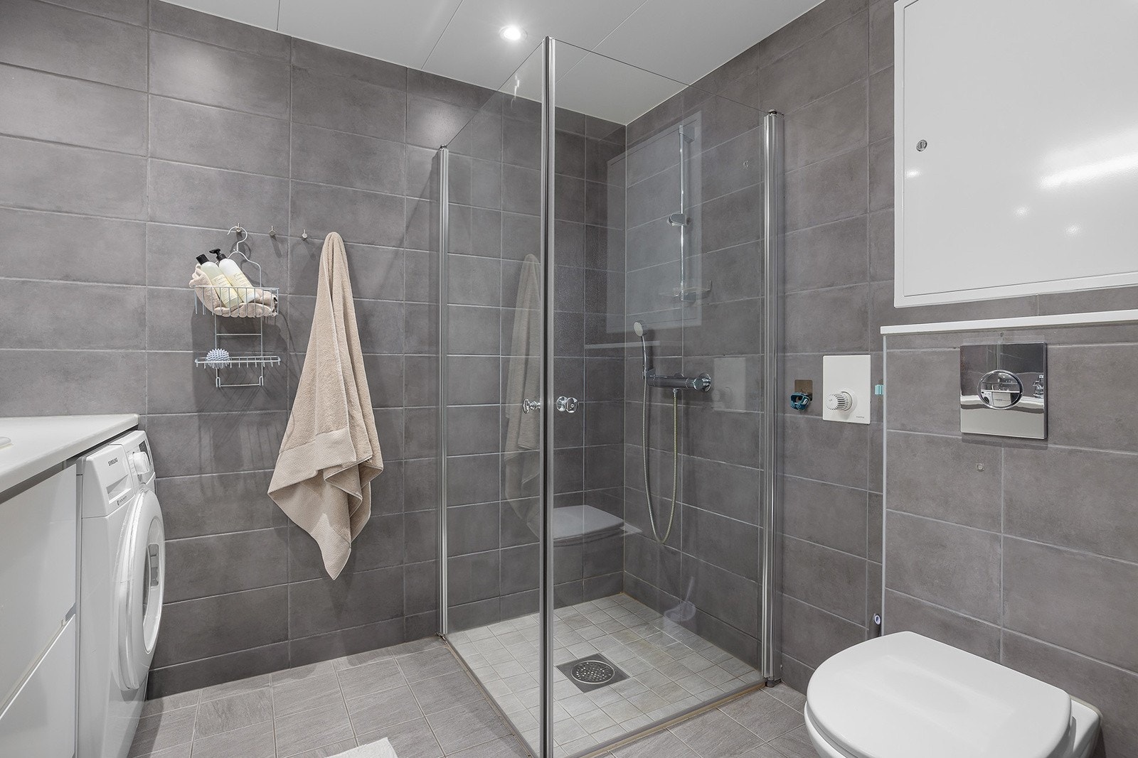 Stilrent og moderne baderom med fliser som skaper et elegant uttrykk. Varme i gulv og downlights i himling. Dusjhjørne med svingbare glassdører og vegghengt toalett. Galleribilde
