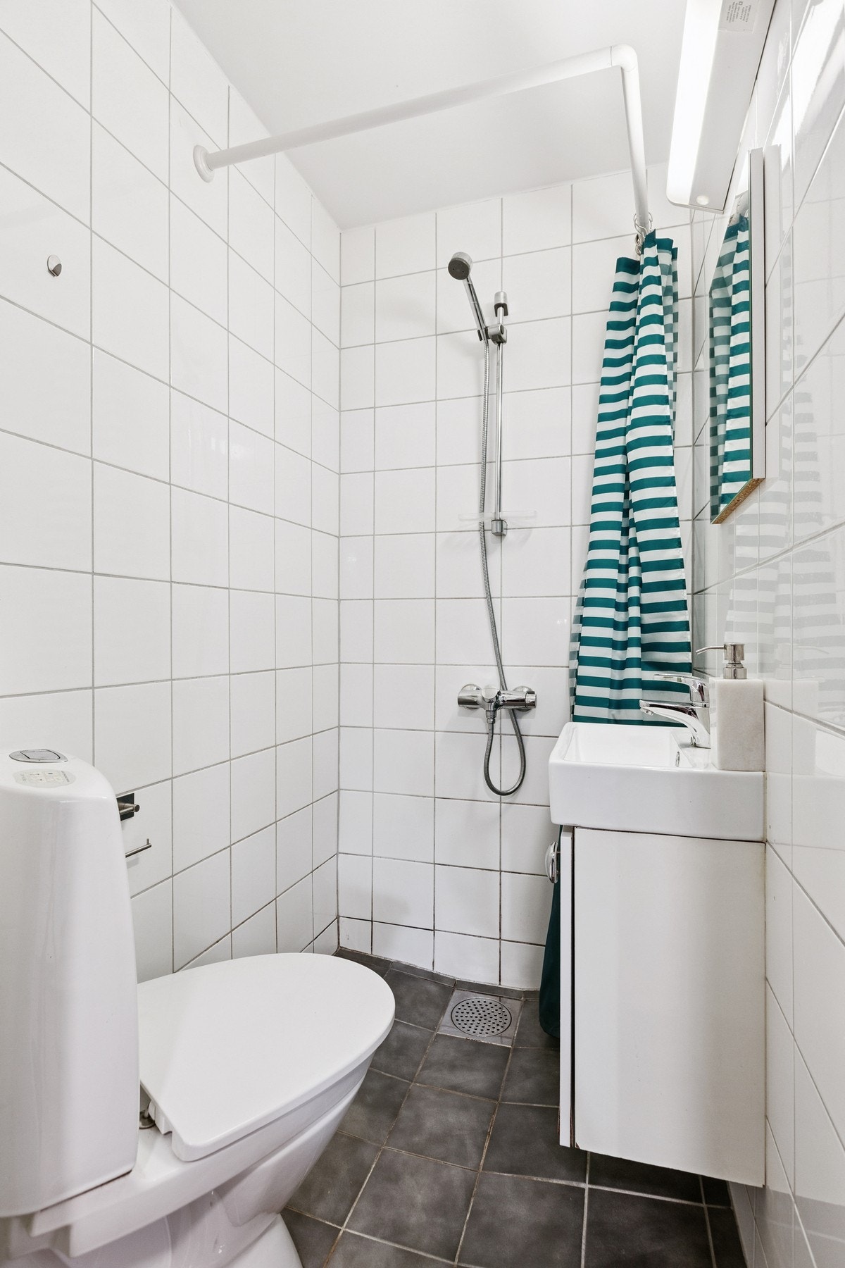 Badet er utstyrt med vegghengt servantinnredning, speil med overlys, vegghengt dusjarmatur og toalett. Galleribilde