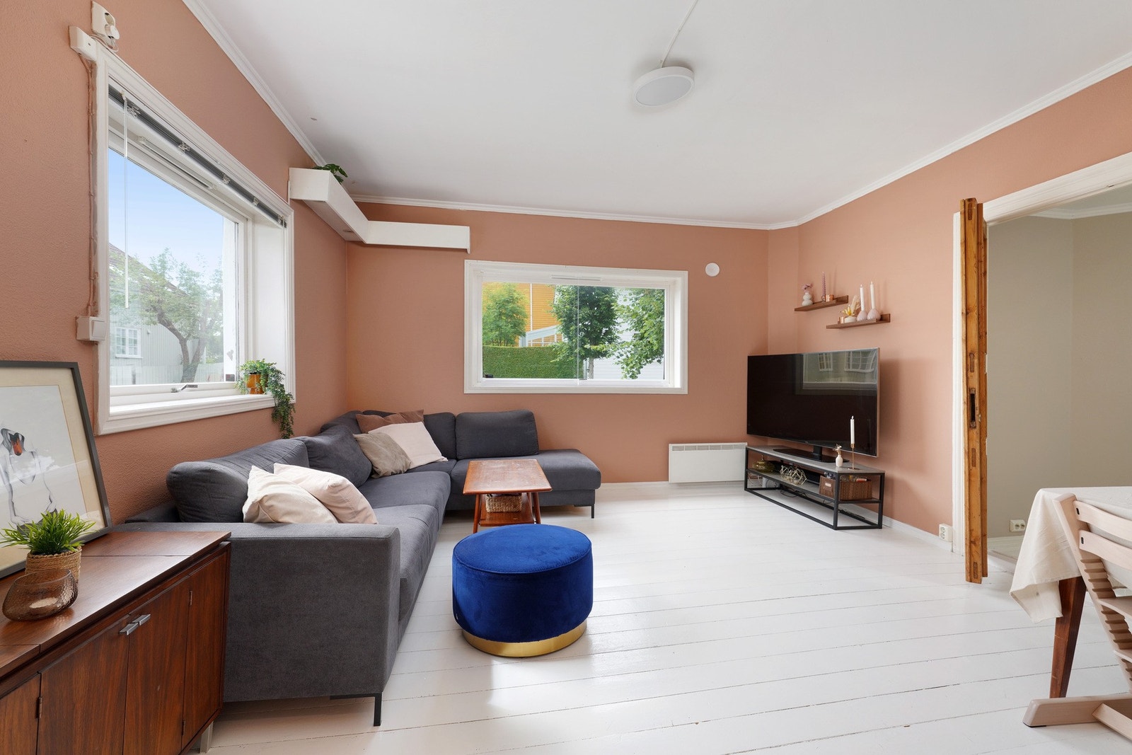 Det originale tregulvet er malt i stuen og det er to store vinduer som gir rikelig med naturlig lys Galleribilde