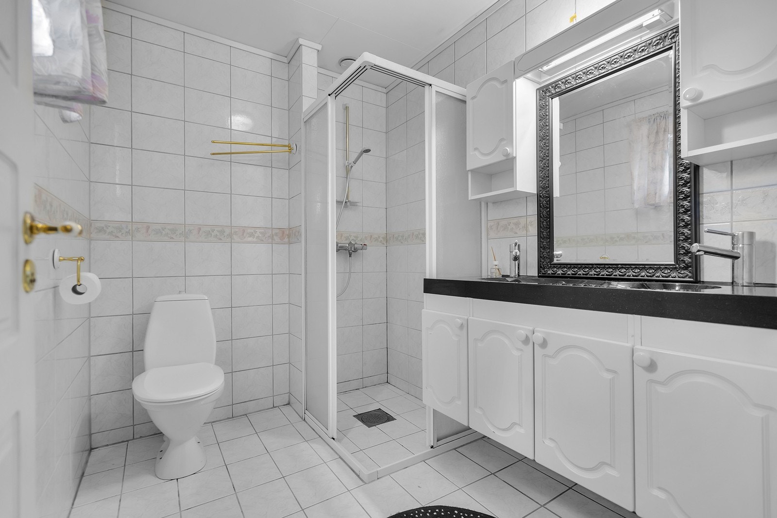 Lyst bad med toalett, dusjhjørne og dobbel servant med oppbevaringsmuligheter. Galleribilde