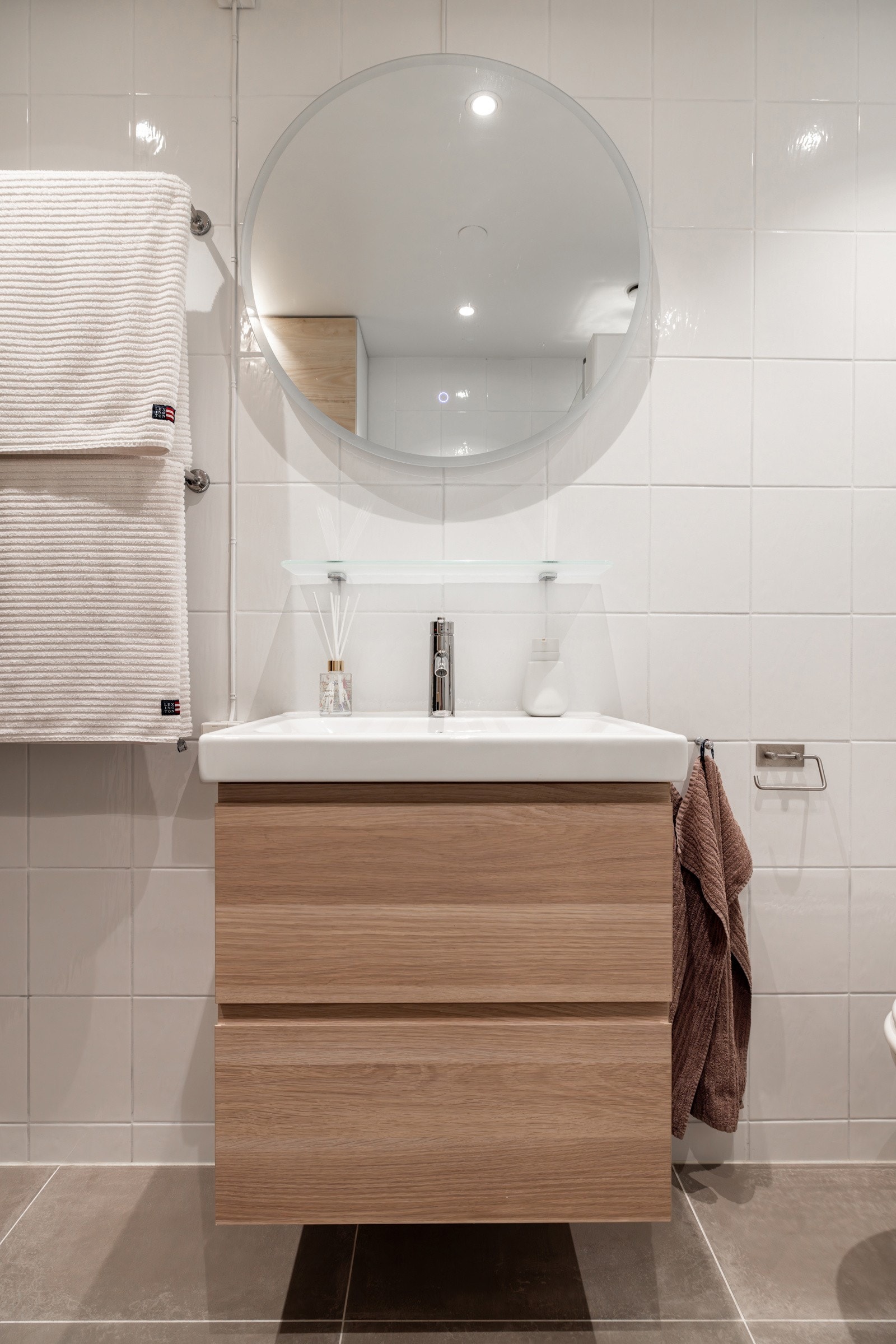 Rommet er innredet med vegghengt servantinnredning med skuffer, ovenpåliggende servant med ett-greps armatur, speil med ledlys, og vegghengt baderomsmøbel med dør og skuffer. Galleribilde