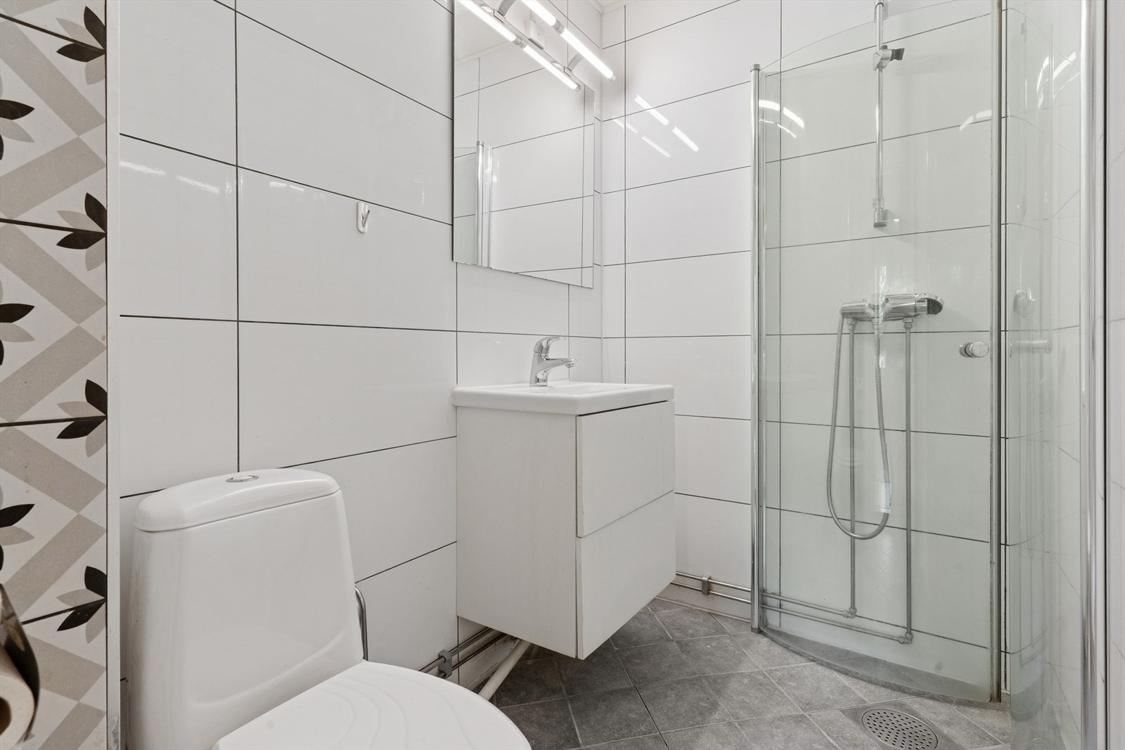 Pent, flislagt bad utstyrt med wc, servant og svingbare dusjvegger av glass. Galleribilde
