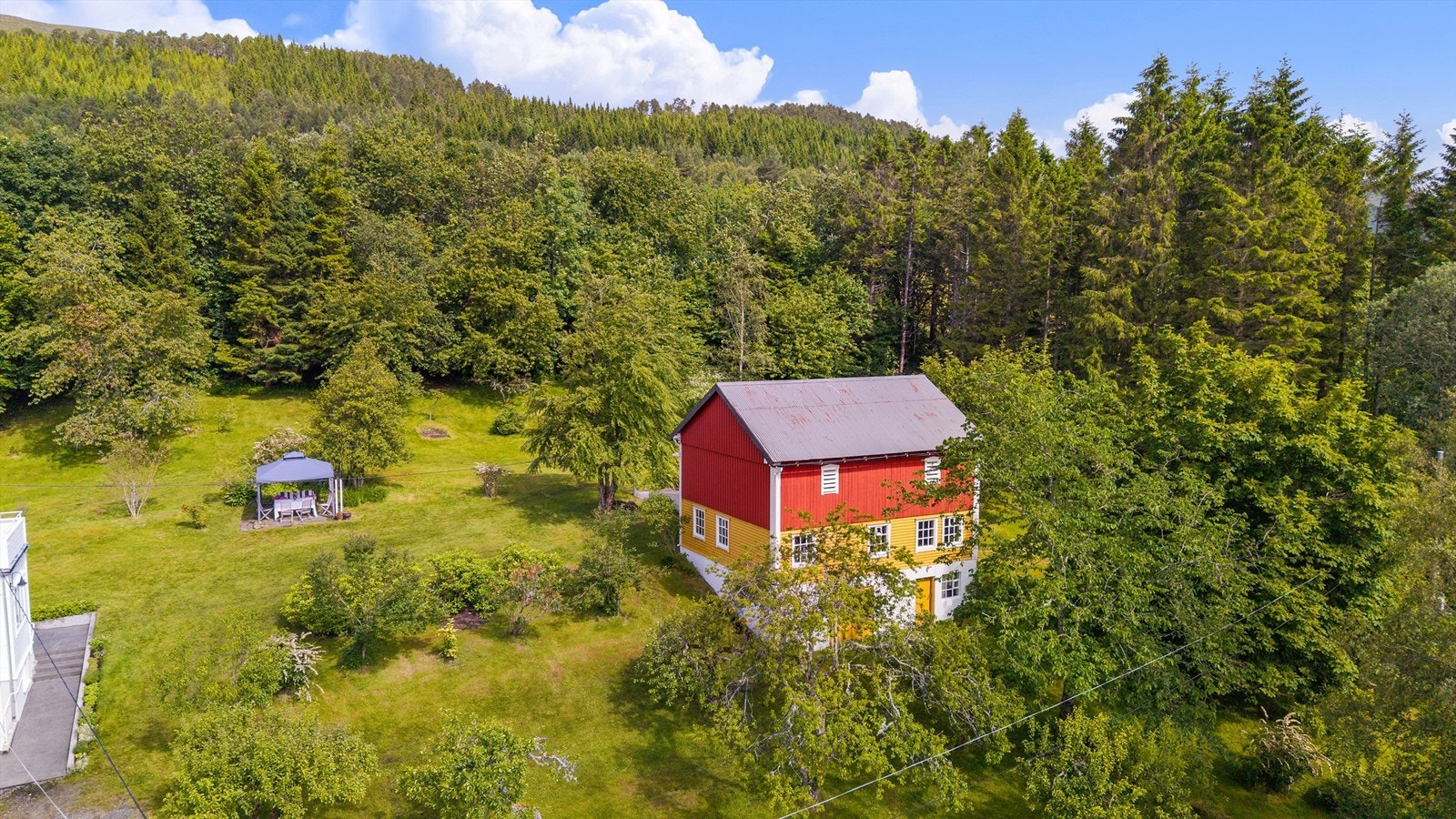 Dronebilde av hagen og låven beliggende øst for bolighuset med solplass i hagen Galleribilde