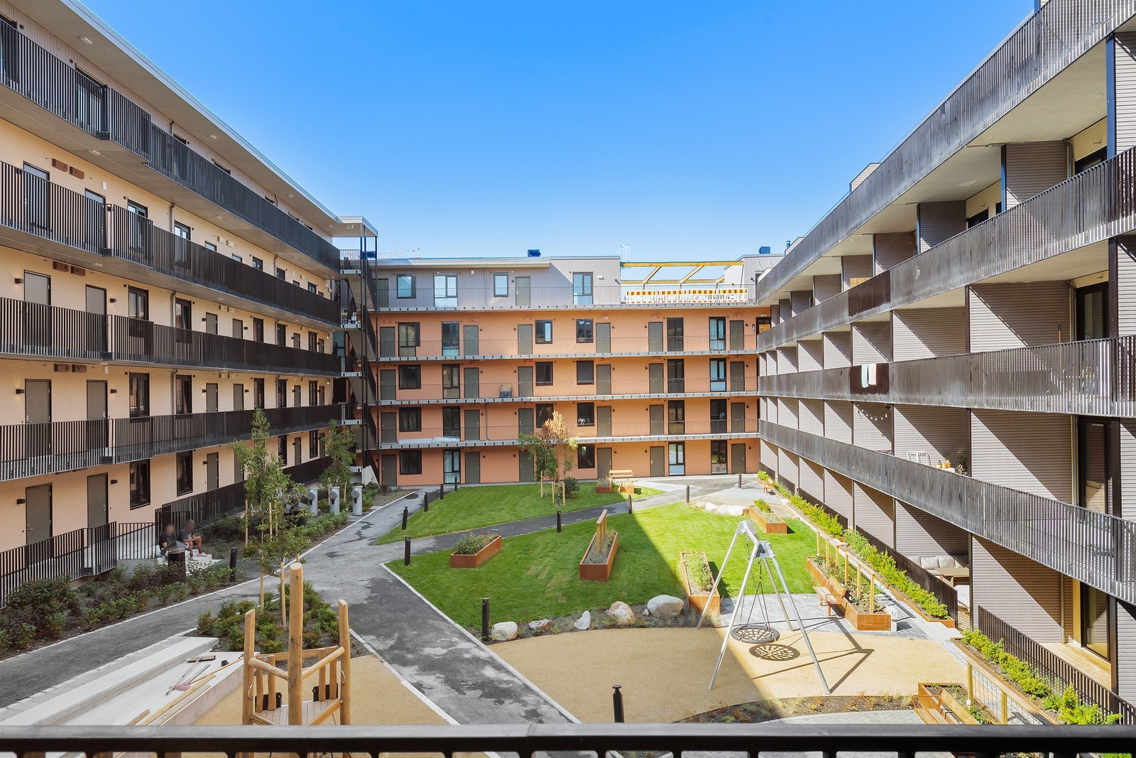 Stor, grønn opparbeidet felleshage i bakgården med blant annet gressplen, sitteplasser og lekestativ Galleribilde