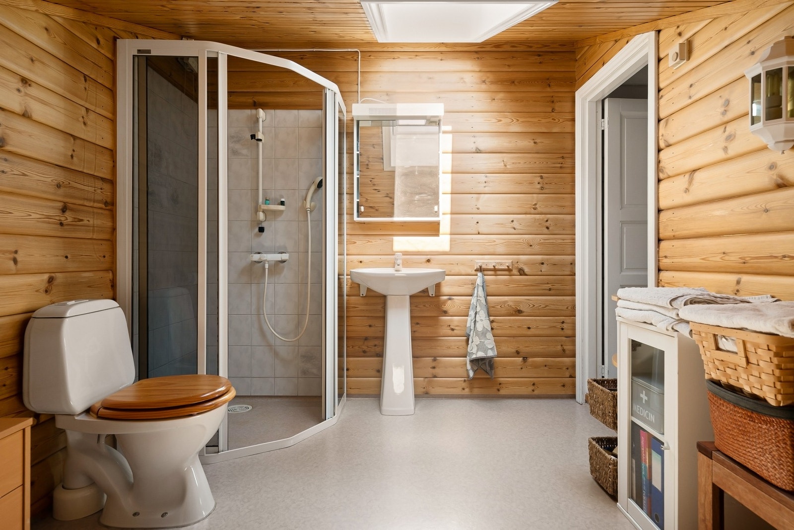 Et av boligens bad har en enkel, men sjarmerende utforming med belegg på gulv, dusjhjørne, klosett og servant - omgitt av varme trevegger som gir en lun og tradisjonell atmosfære. Galleribilde