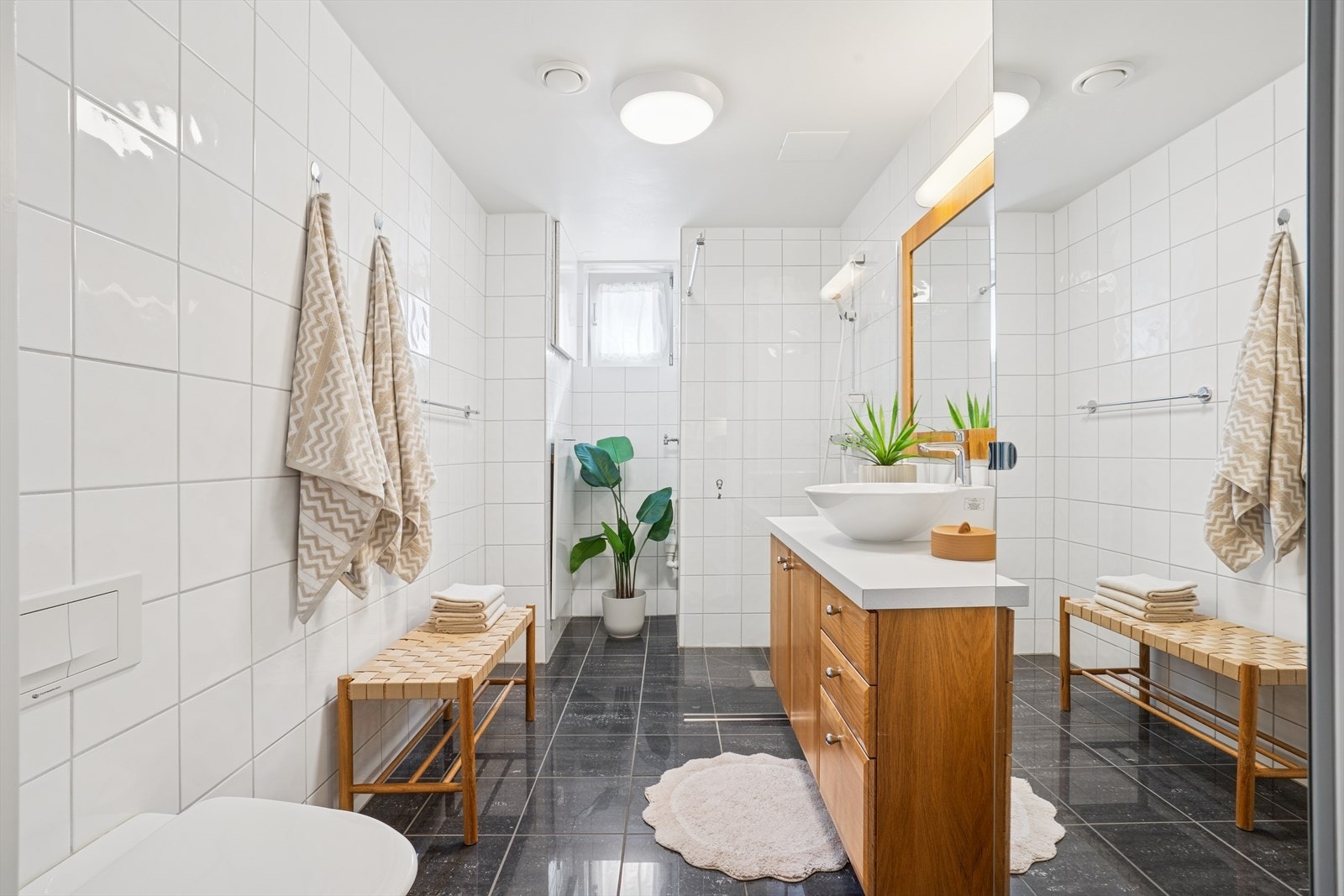 Badet er moderne og funksjonelt, med flislagte overflater, vegghengt toalett, servant og opplegg for vaskemaskin. Galleribilde