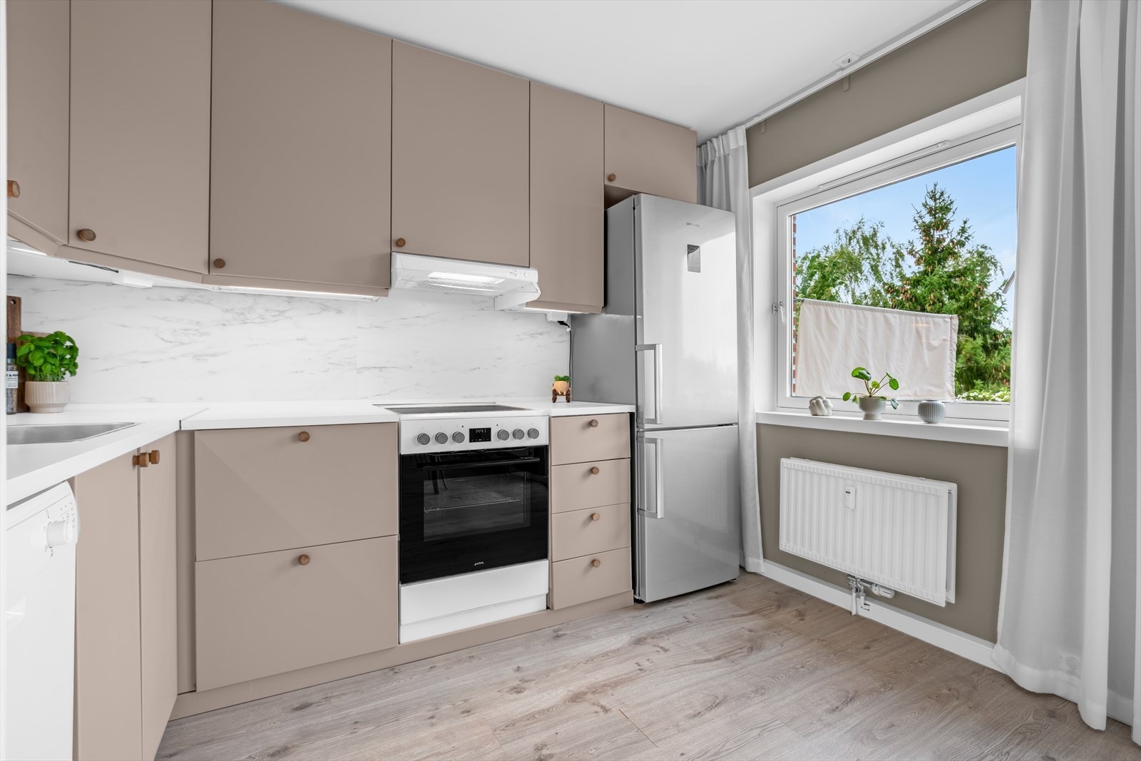 Kjøkkeninnredningen består av glatte, folierte fronter, laminat benkeplate (2024) med nedfelt kum i rustfritt stål og ledlys under overskap. Galleribilde
