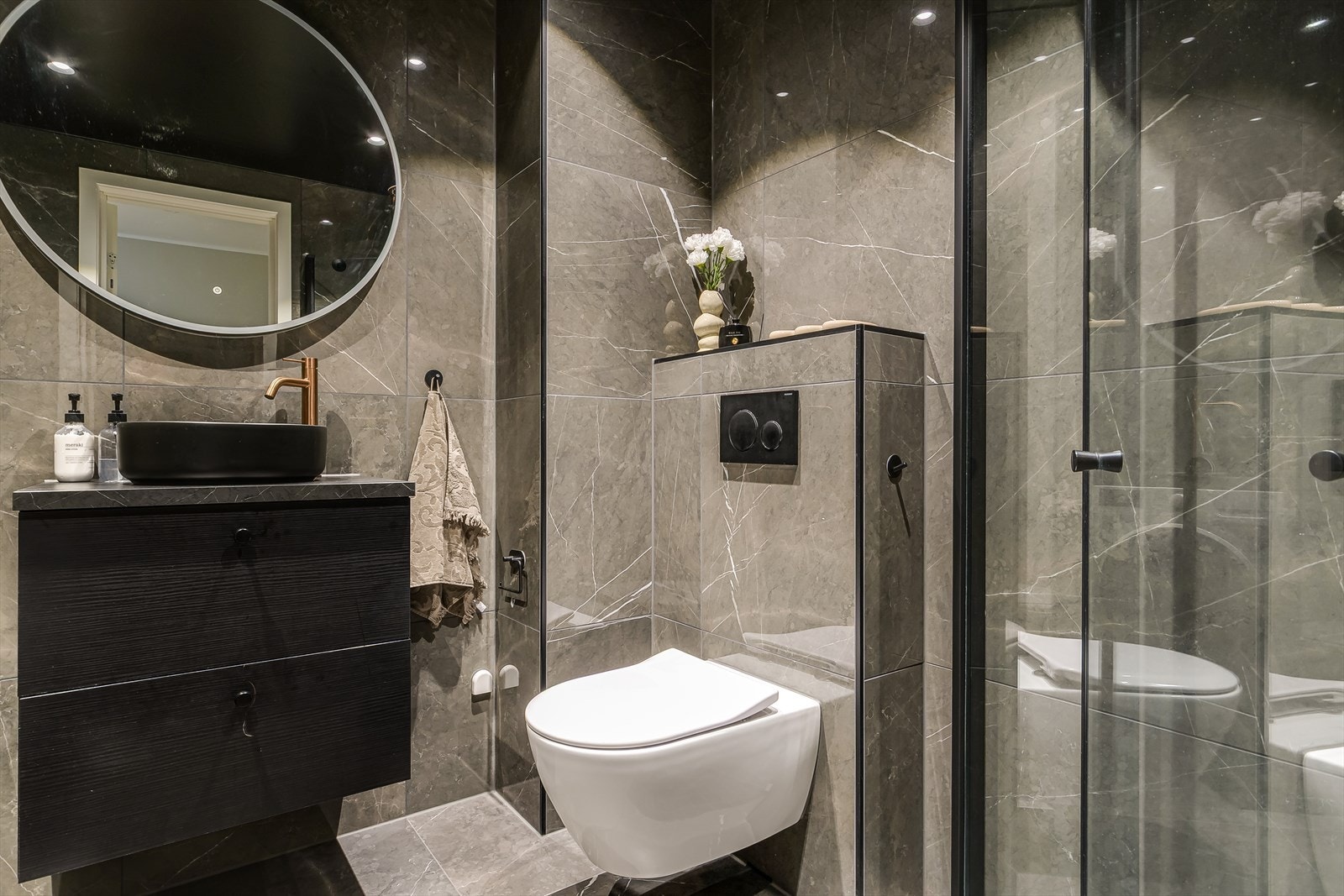 Rommet er innredet med dusjnisje, speil med sminkelys, servant med innredning, opplegg for vaskemaskin under benkeplate med skap, og vegghengt toalett Galleribilde