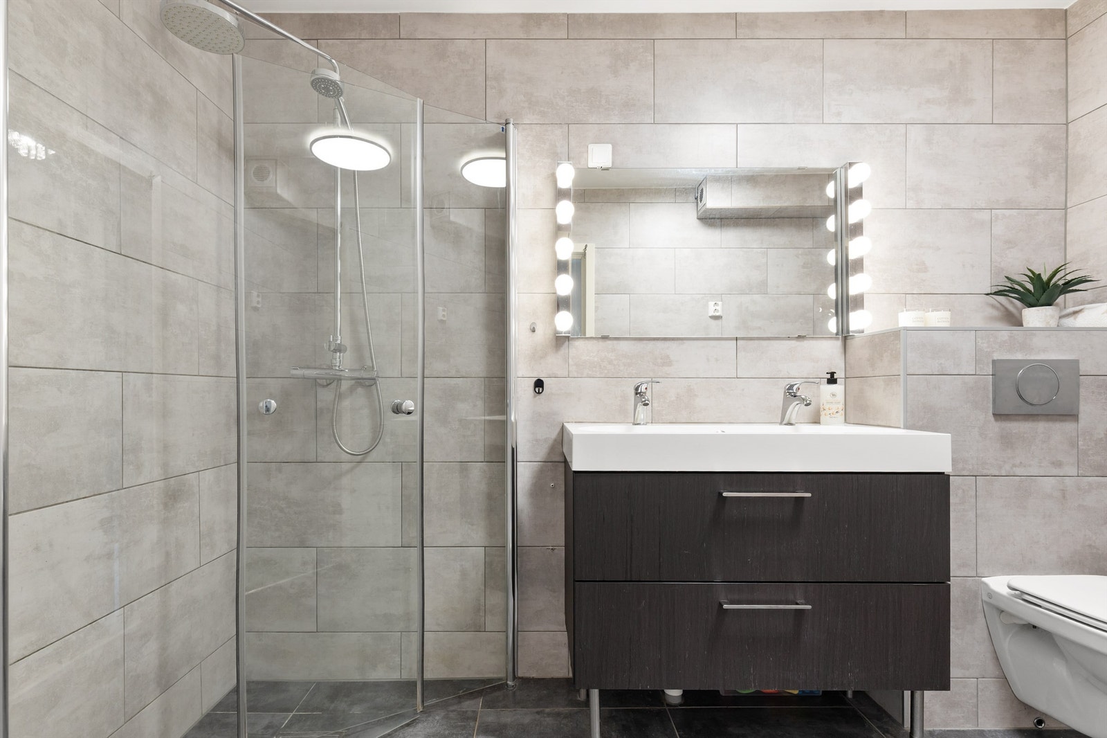 Badet er innredet med vegghengt klosett, baderomsinnredning med heldekkende servant, speil med belysning og dusjhjørne med svingbare glassdører. Galleribilde