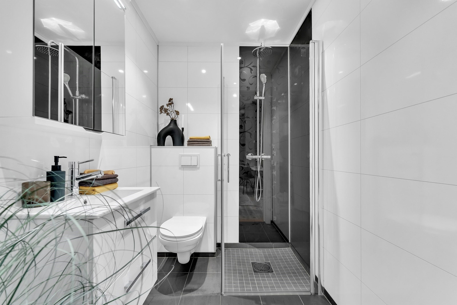 Innredet med vegghengt servantinnredning, speil med lys og dusjhjørne med innfellbare glassvegger. Vegghengt toalett. Galleribilde