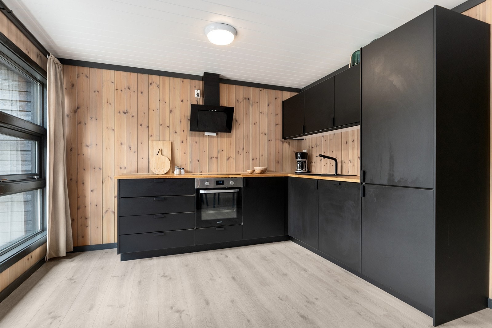 Stilrent kjøkken med slette, sorte fronter med benkeplate i heltre og integrerte hvitevarer. Galleribilde