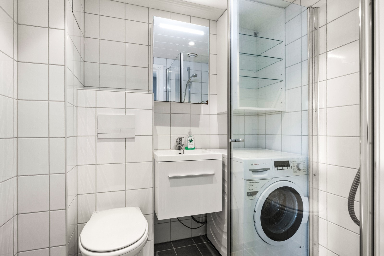 Pent flislagt bad med dusjhjørne og opplegg for vaskemaskin. Galleribilde