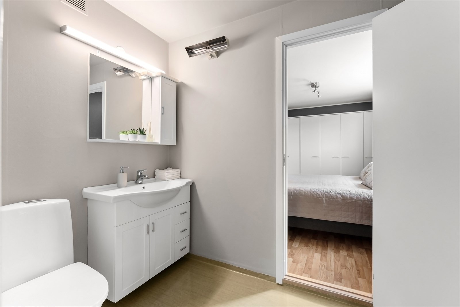 Badet innenfor soverommet er møblert med toalett servant i innredning og speil med sideskap i tillegg til dusjkabinett. Galleribilde