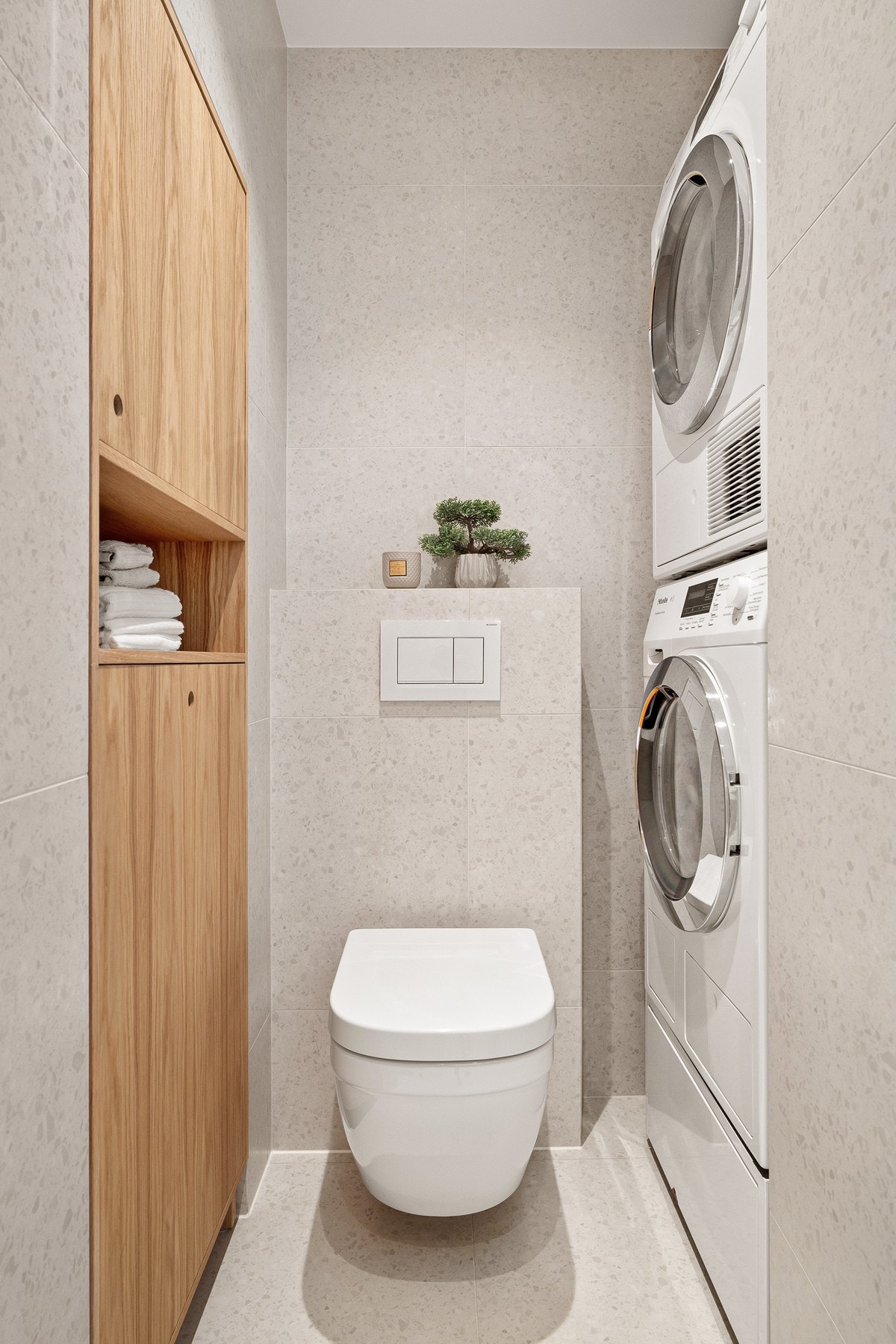 Vegghengt toalett med innebygd sisterne. I hjørne er det lagd til en superpraktisk nisje med vaskesøyle for vaskemaskin og tørketrommel, samt plasstilpasset veggskap i eik, som gir ekstra oppbevaring. Badet har også elektrisk styrt avtrekksvifte. Galleribilde