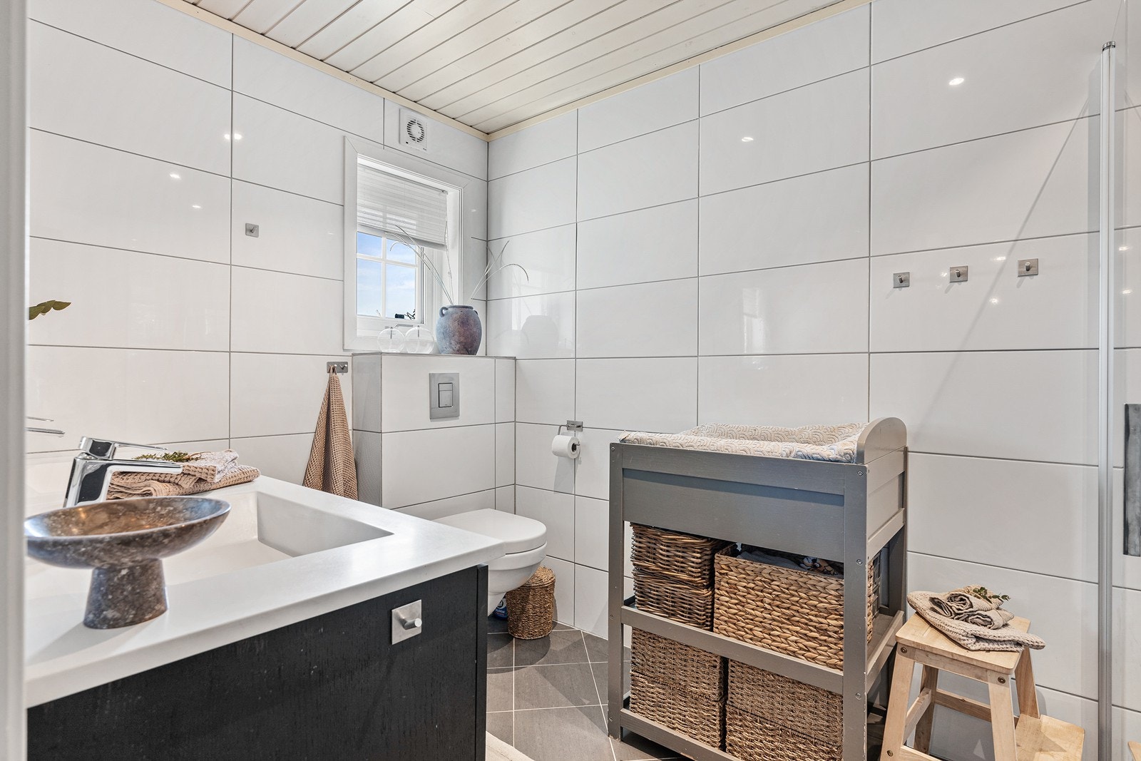 Badet er innredet med toalett, dusjvegger i glass, samt skapinnredning og skuffeinnredning med dobbel vask og speil. Galleribilde