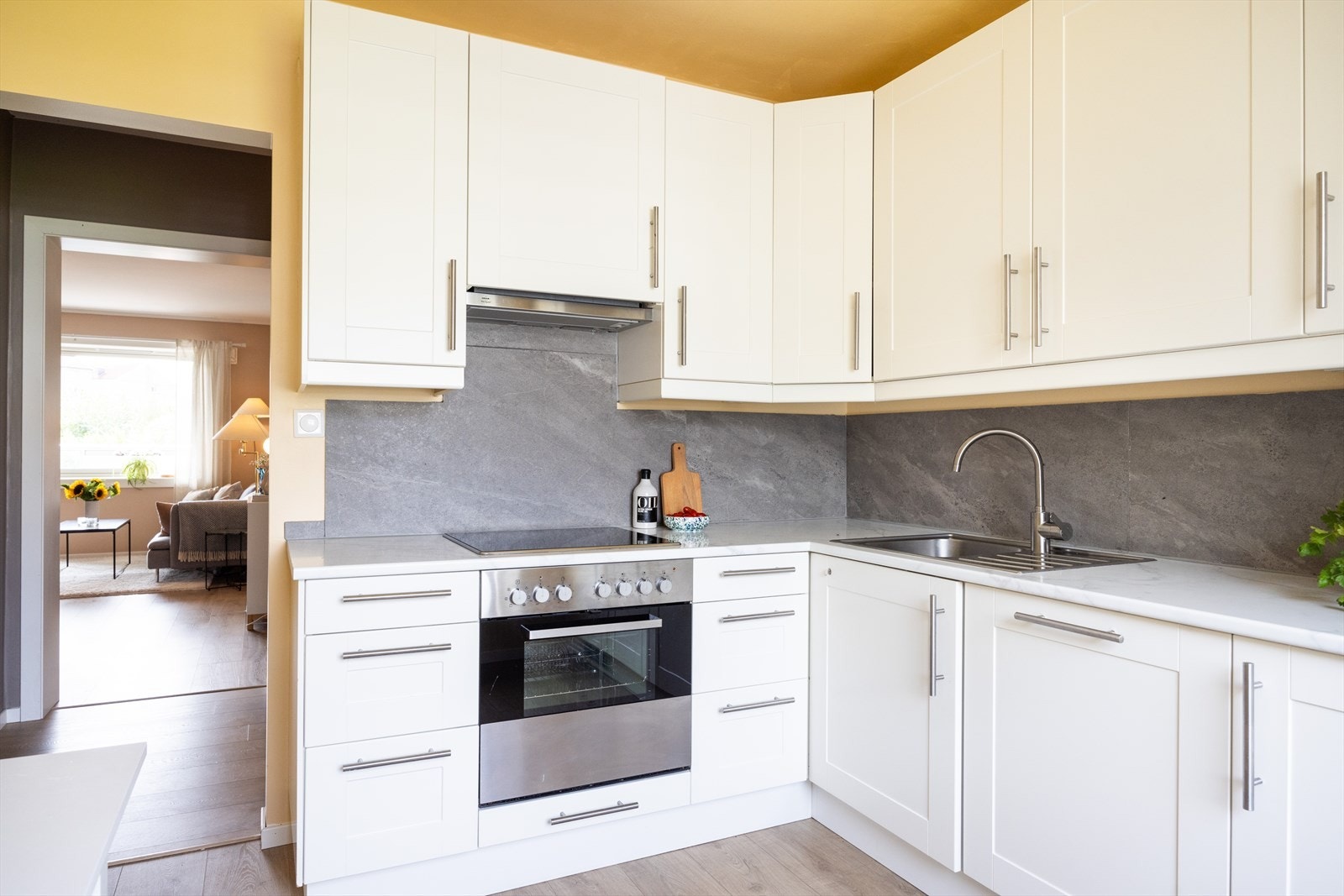 Kjøkkeninnredningen består av hvite, profilerte fronter og benkeplate av laminat med nedfelt kum i rustfritt stål. Galleribilde