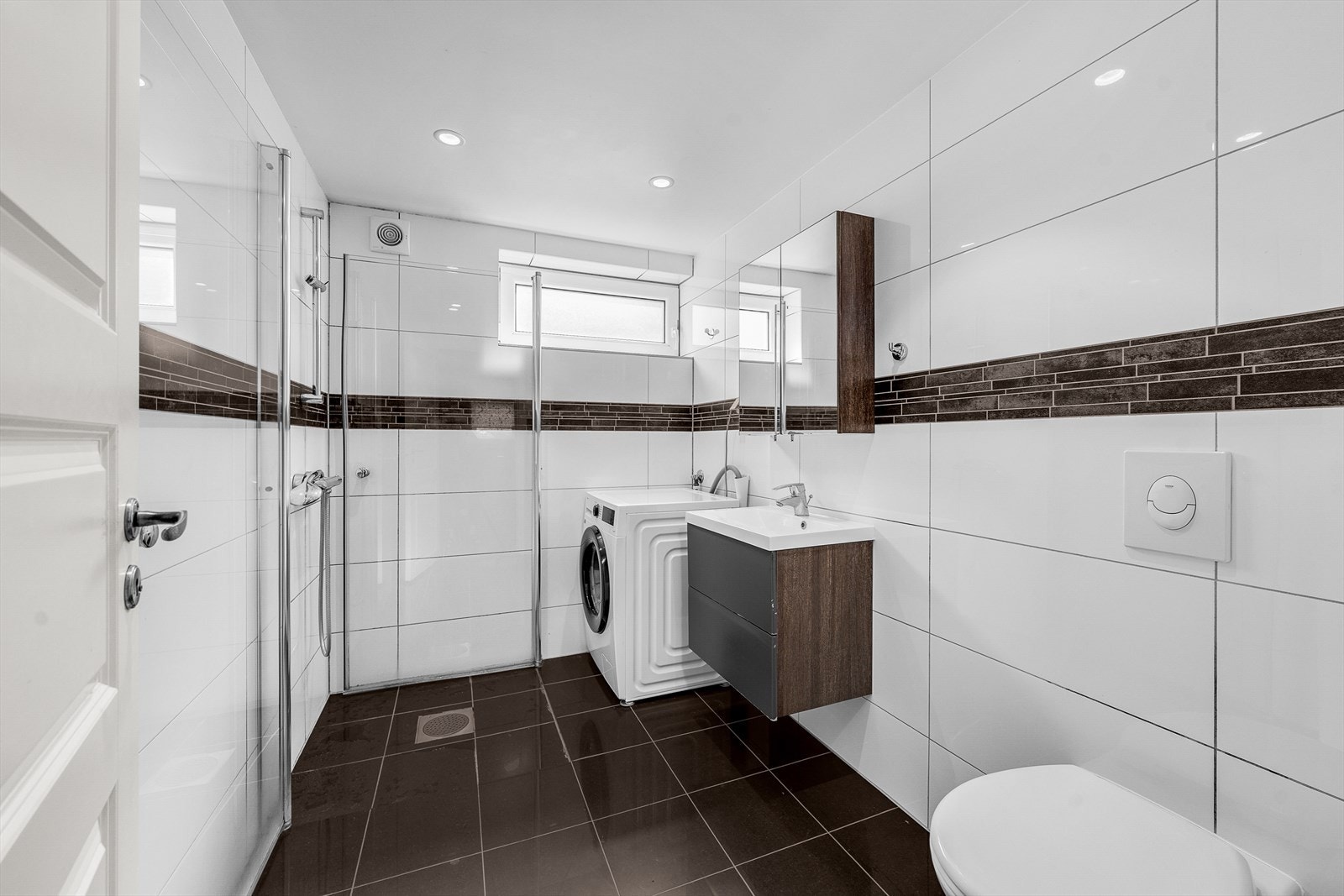 Delikat bad fra 2015 med flislagte overflater, dusjhjørne og opplegg for vaskemaskin. Galleribilde