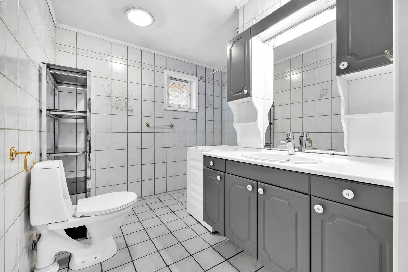 Badet er av endre dato og er utstyrt med vegghent servantskap med profilerte fronter på skap og skuffer, benkeplate i laminat og nedsenket servant med ett-greps armatur. Galleribilde