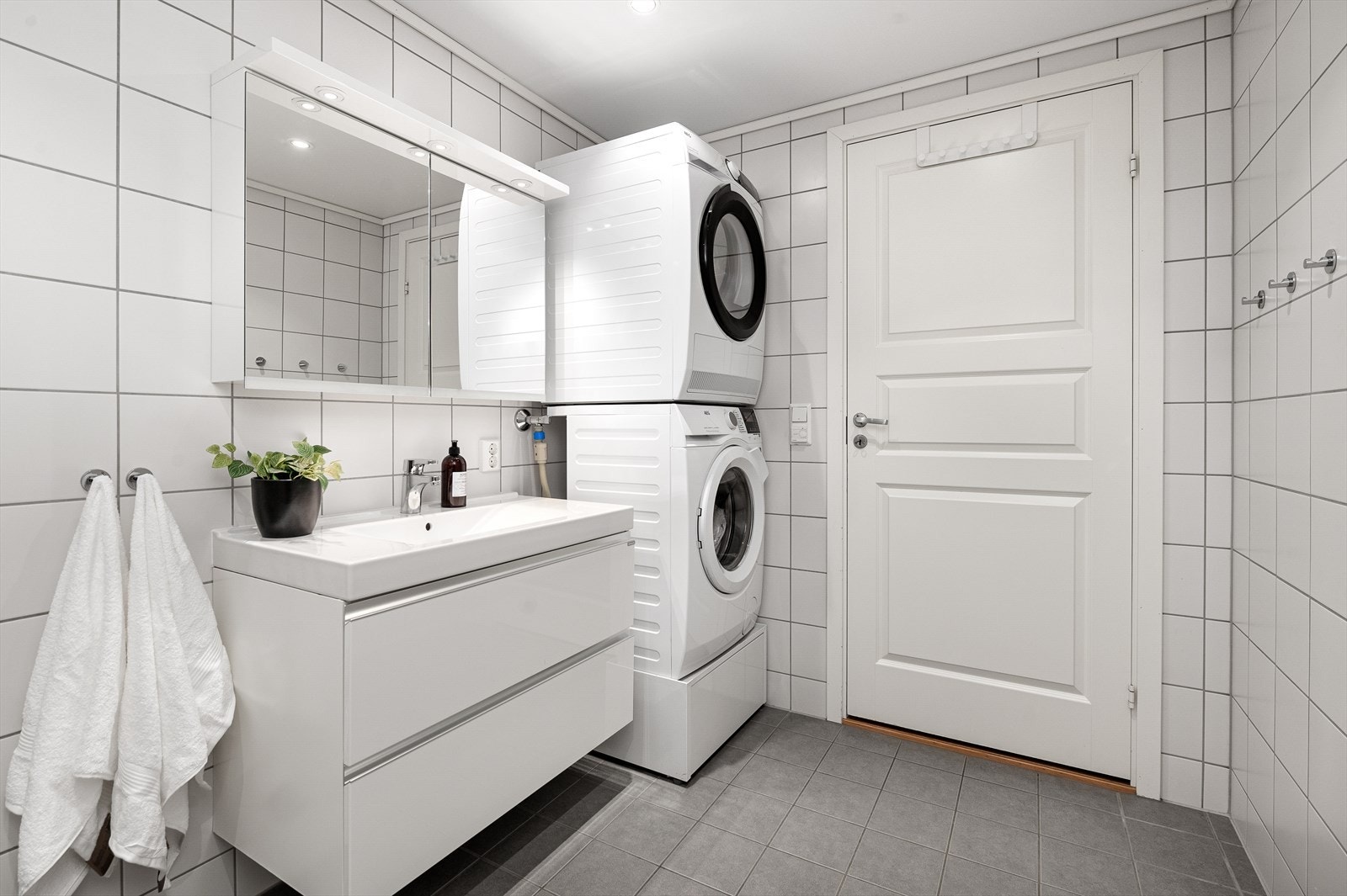 Badet er utstyrt med dusjvegger av glass og dusjgarnityr på vegg, vegghengt toalett, praktisk innredning med servant og opplegg for vaskemaskin Galleribilde