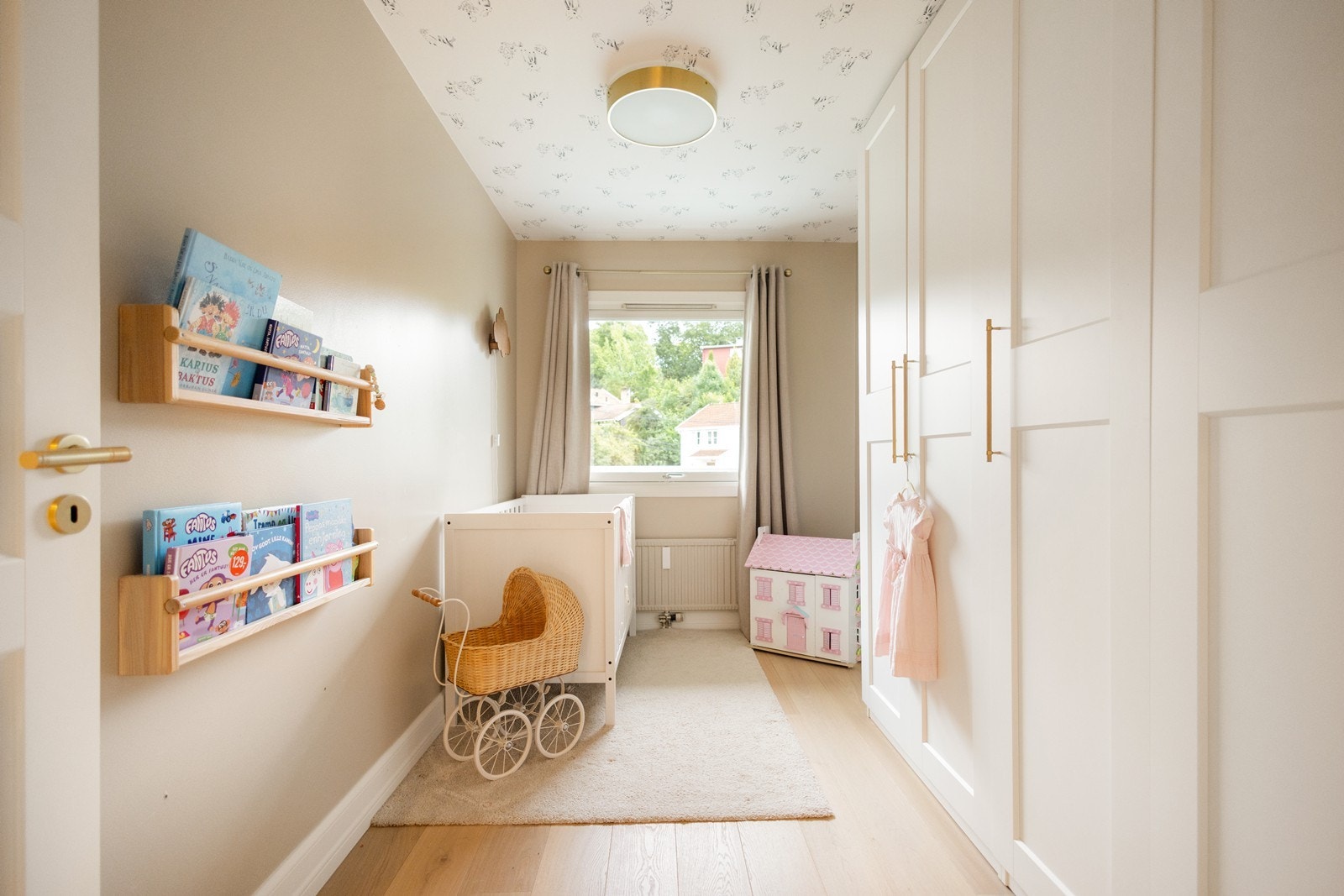 Lyst og delikat barnerom nummer to med leken tapet i taket, store garderober med messinghåndtak og plass til seng og lekeområde Galleribilde