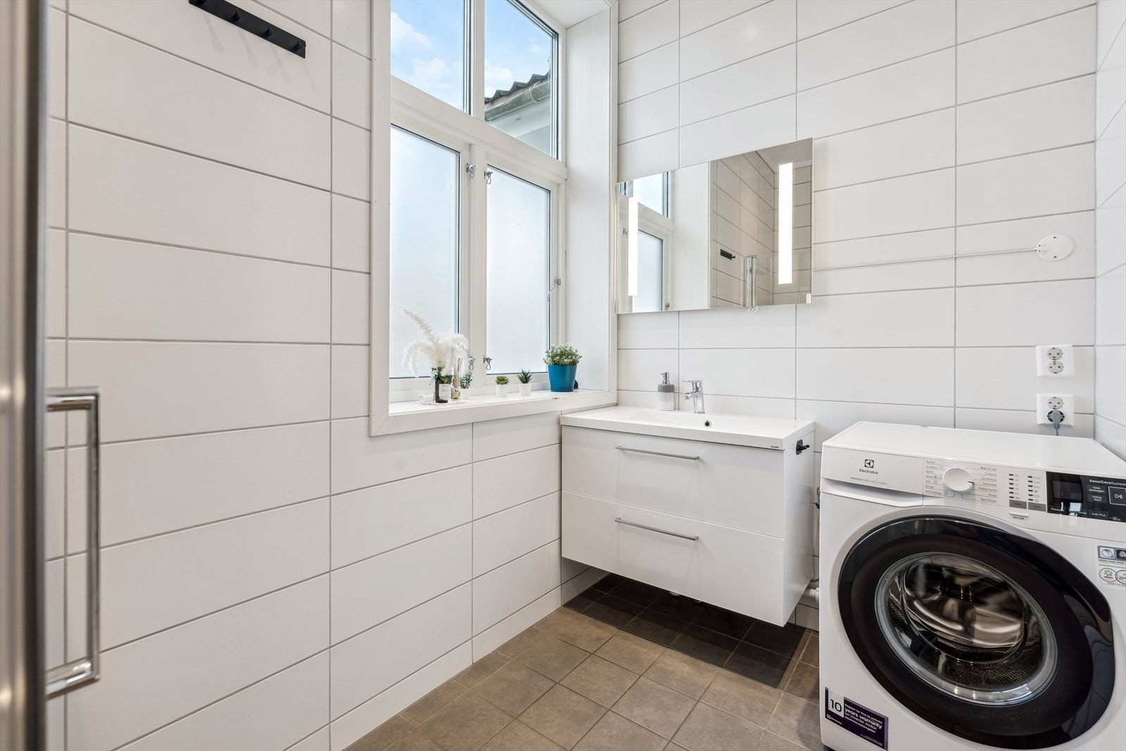 Lekkert flislagt bad med dusjnisje, wc, pen innredning og opplegg for vaskemaskin Galleribilde