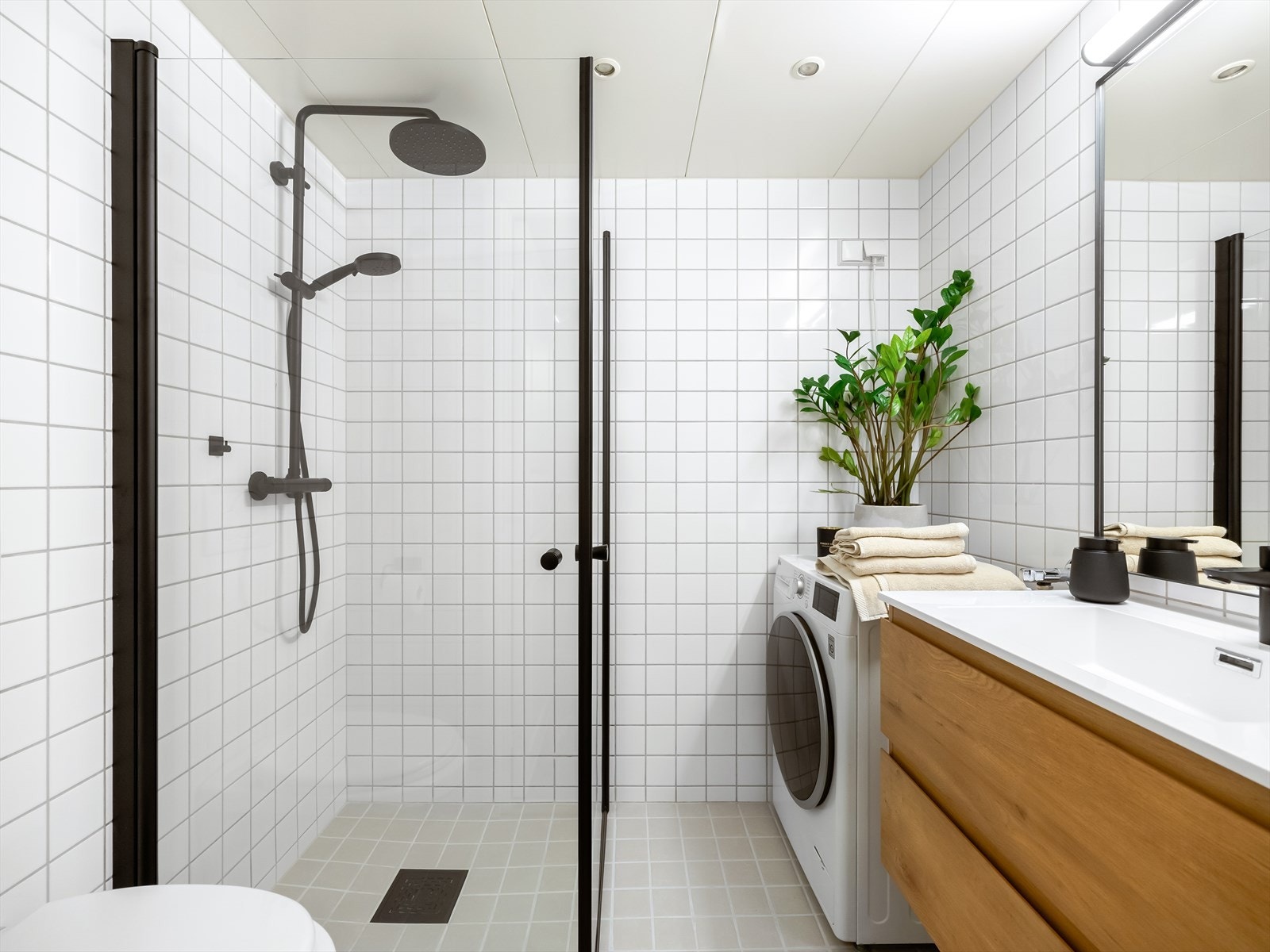 Delikat og romslig baderom bestående av servantinnredning med skuffer og speil, vegghengt toalett og dusj med glassdører. Galleribilde