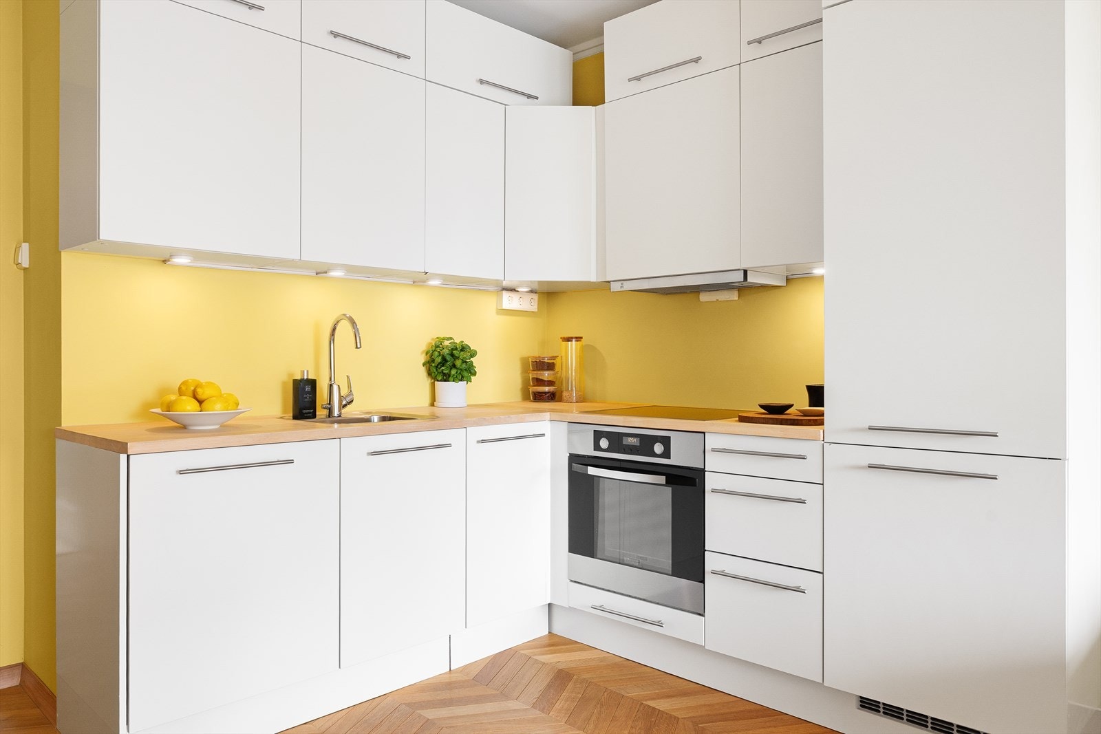 Innredningen har hvite, matte fronter, lys under overskap og heltre benkeplate med oppvaskkum. Galleribilde