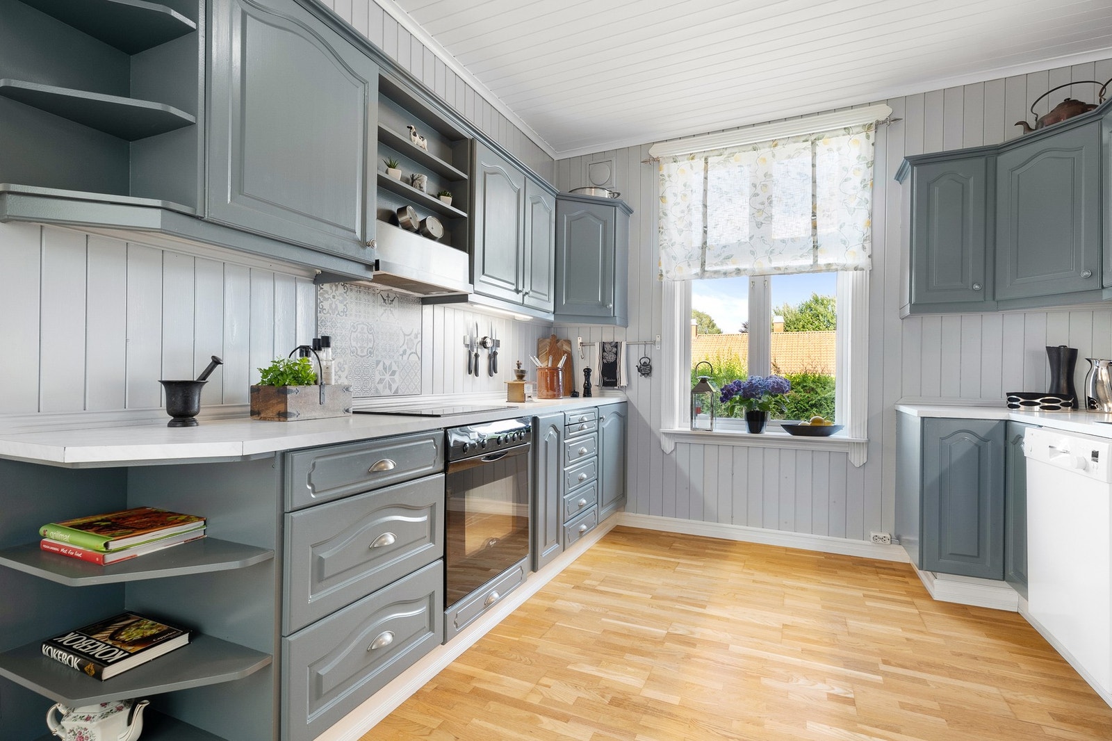 Innredningen er oppført langs to vegger, med grå, profilerte fronter, vitrineskap og oppvaskkum nedfelt i en laminert benkeplate. Galleribilde