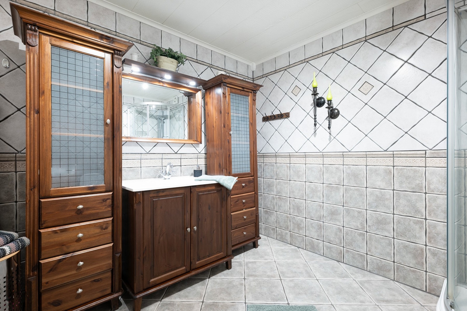 I første etasje har boligen et romslig bad. Baderomsinnredningen har et klassisk uttrykk, bestående av heldekkende servant med mørke underskap, to matchende høyskap med glassfronter og et speil med belysning over servanten. Galleribilde