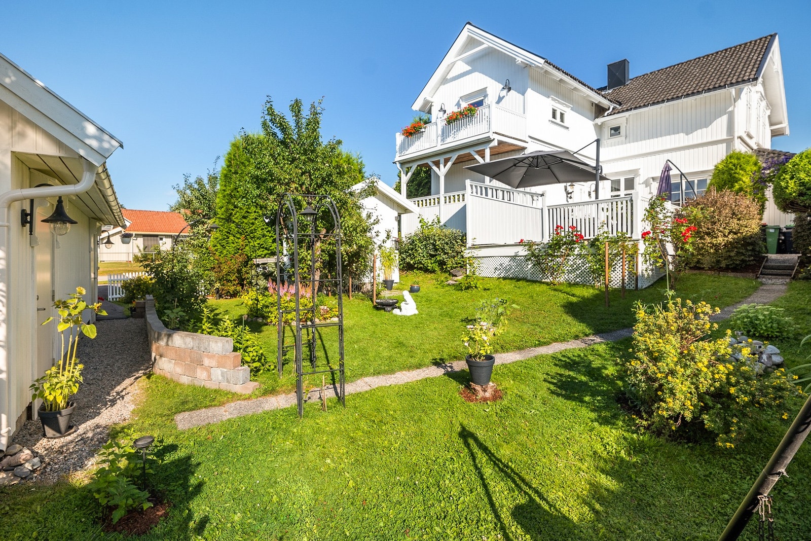 Hagen er skjermet og pent opparbeidet med trær, busker, blomster, gressplen, steinlagte gangstier og diverse beplantning. Et drivhus understreker idyllen, og hagen rammes fint inn av en hekk og et hvitmalt stakittgjerde. Galleribilde