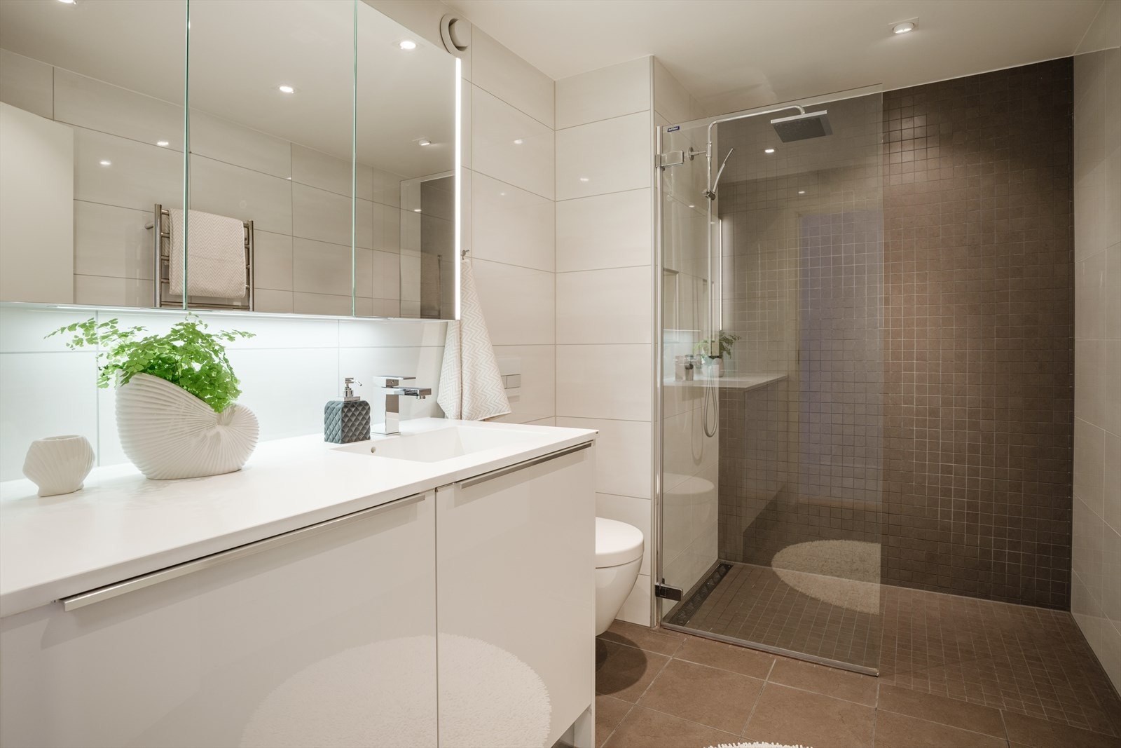 Her er det en dusj med glassdør, vegghengt toalett med demper på dolokket, formstøpt servant med underskap og opplegg for vaskemaskin. Mekanisk avtrekk via en eksternt vifte. Galleribilde