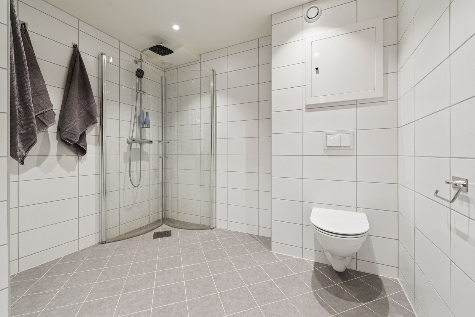 Badet inneholder et vegghengt toalett, en heldekkende servant med blandebatteri, samt et overskap med speil og belysning. Galleribilde