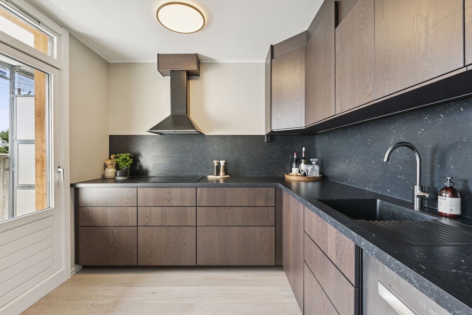 Kjøkkenet har moderne, slette fronter, et praktisk laminat-backsplash og belysning over den stilige benkeplaten. Galleribilde