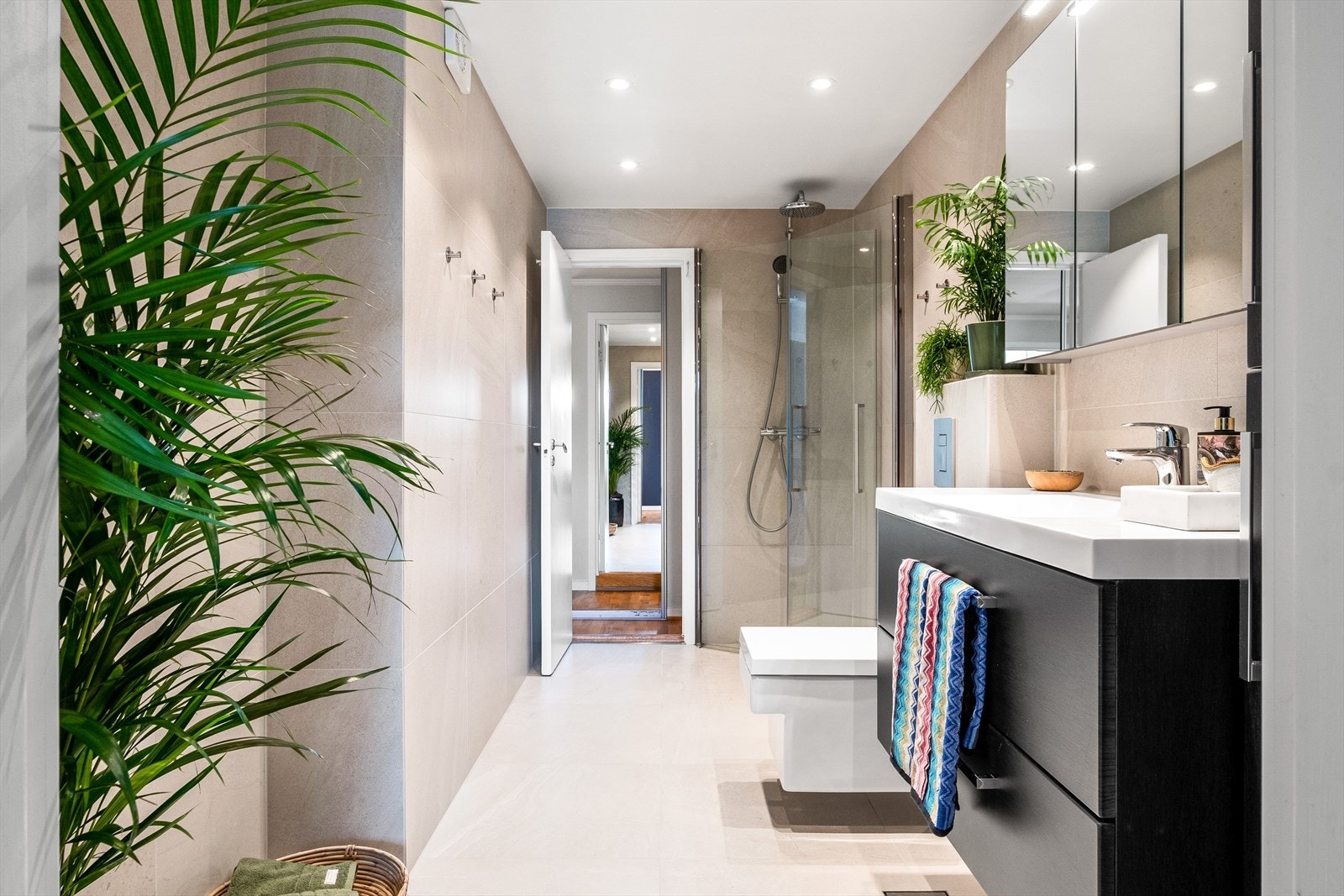 Badet er innredet med servant med underskuffer, overskap med speildører og overbelysning, høyskap, vegghengt toalett og dusjhjørne med glassdører og armatur på vegg. Galleribilde