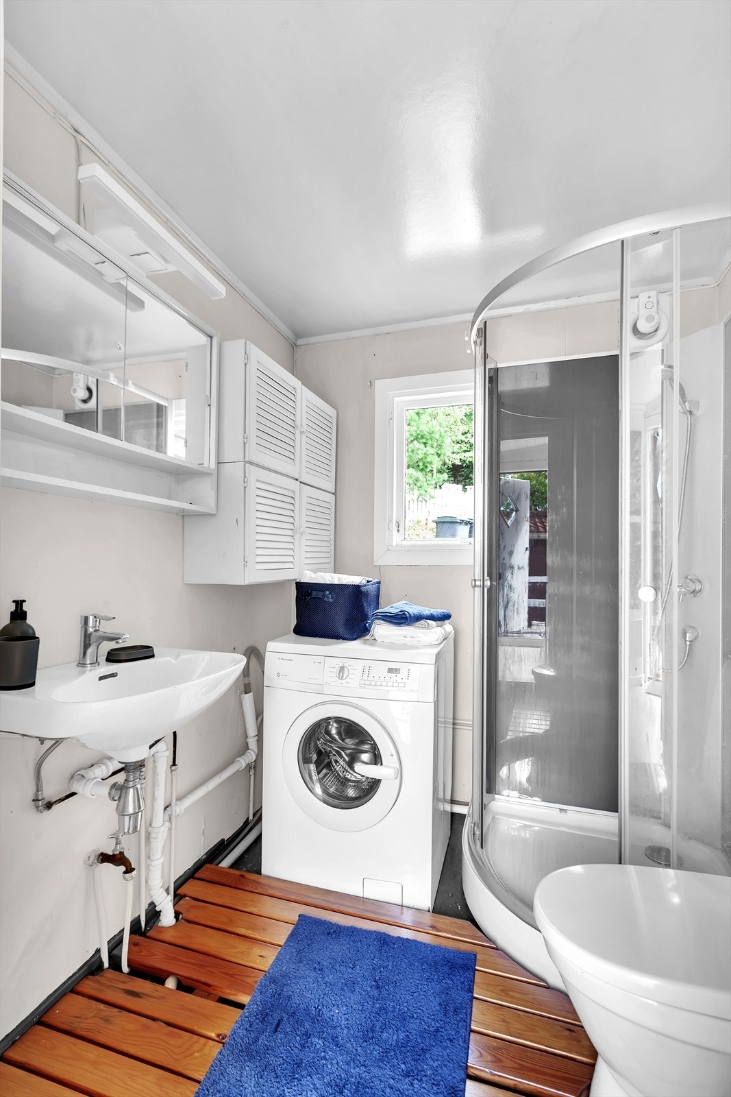 Badet er utstyrt med gulvstående toalett, dusjkabinett, servant og speilskap. Det er opplegg for vaskemaskin. Galleribilde