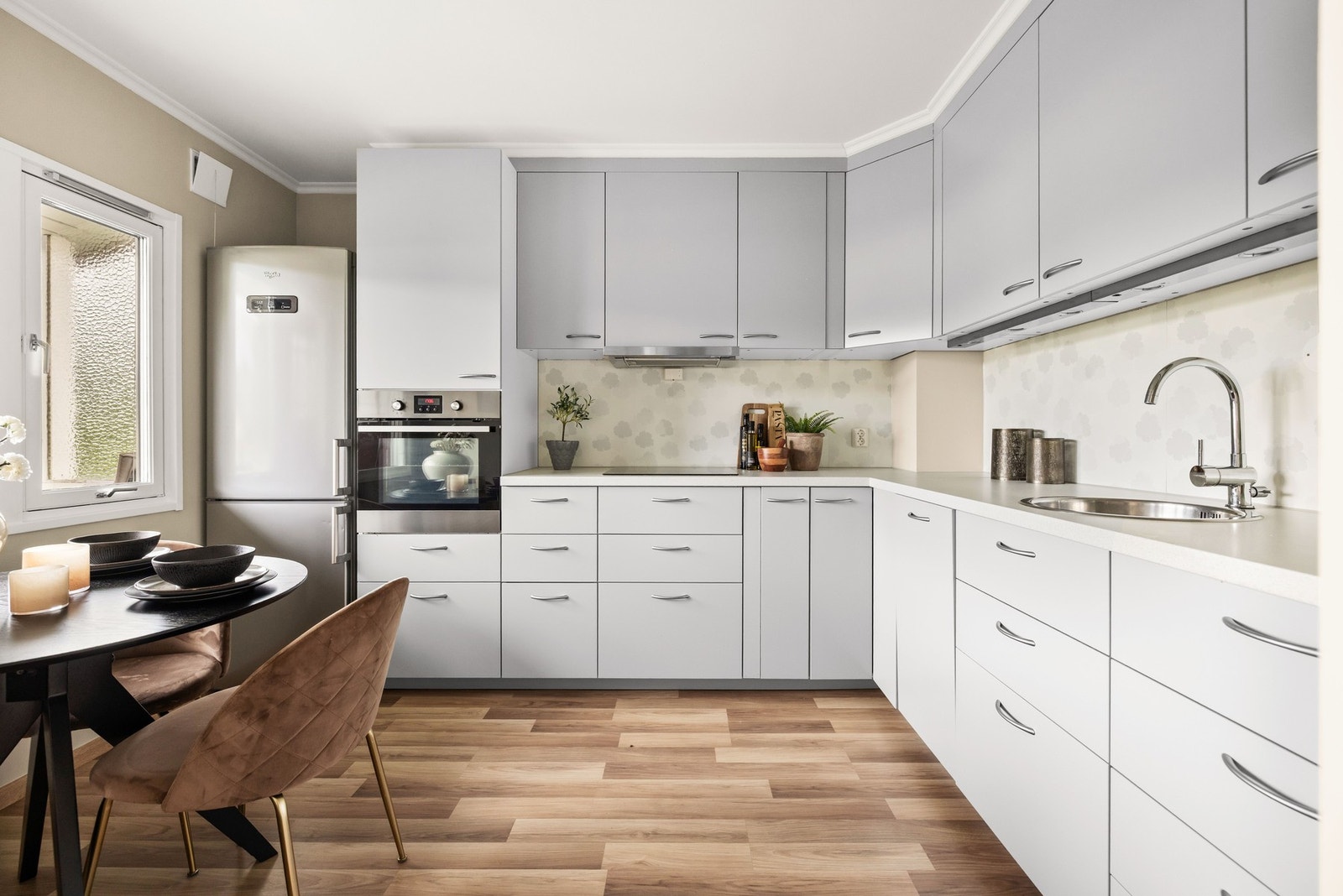 Flott kjøkken med integrerte hvitevarer og spiseplass ved vinduet Galleribilde